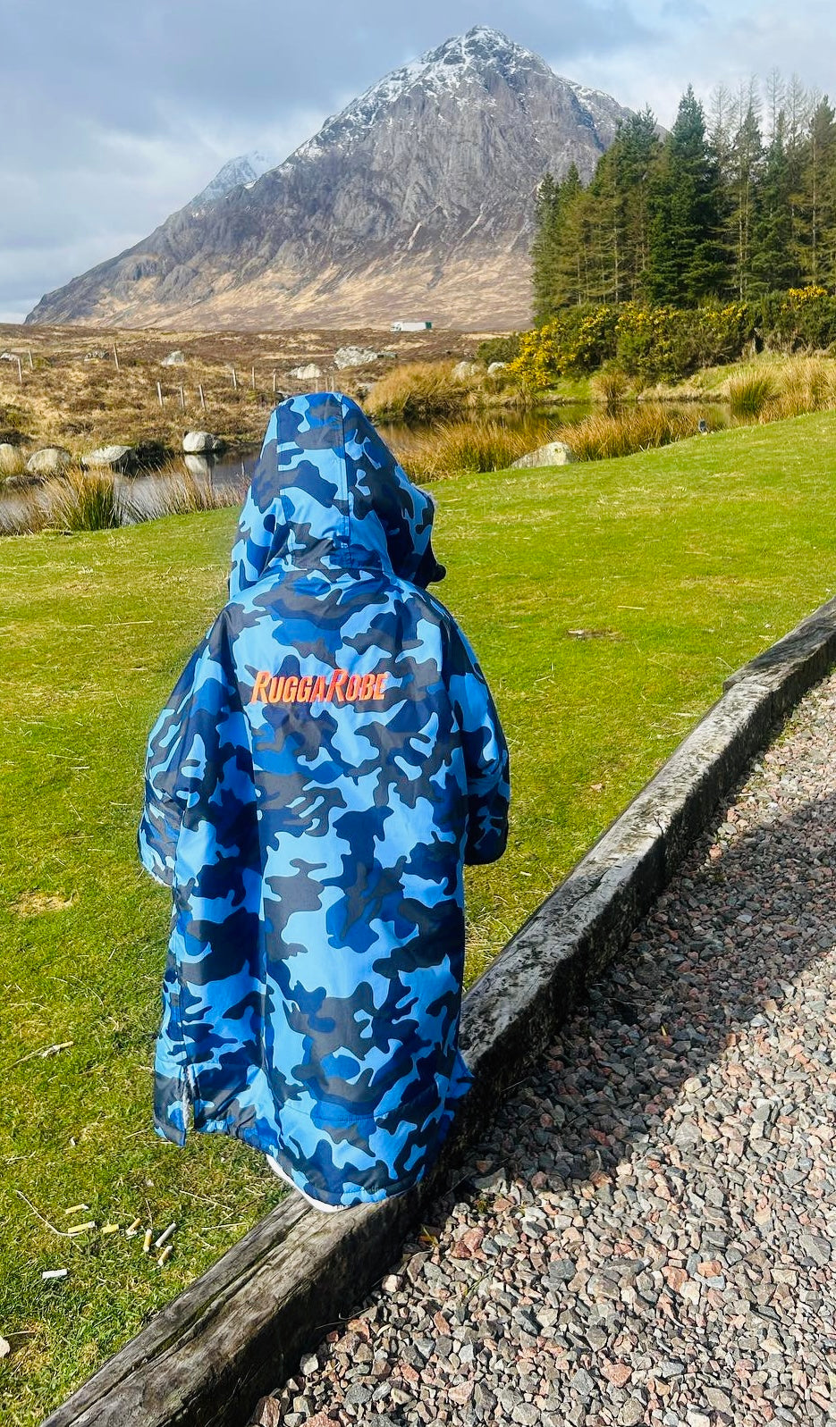 Model wearing RuggaRobe blue camo change robe with grey fleece interior in countryside with mountain in the background