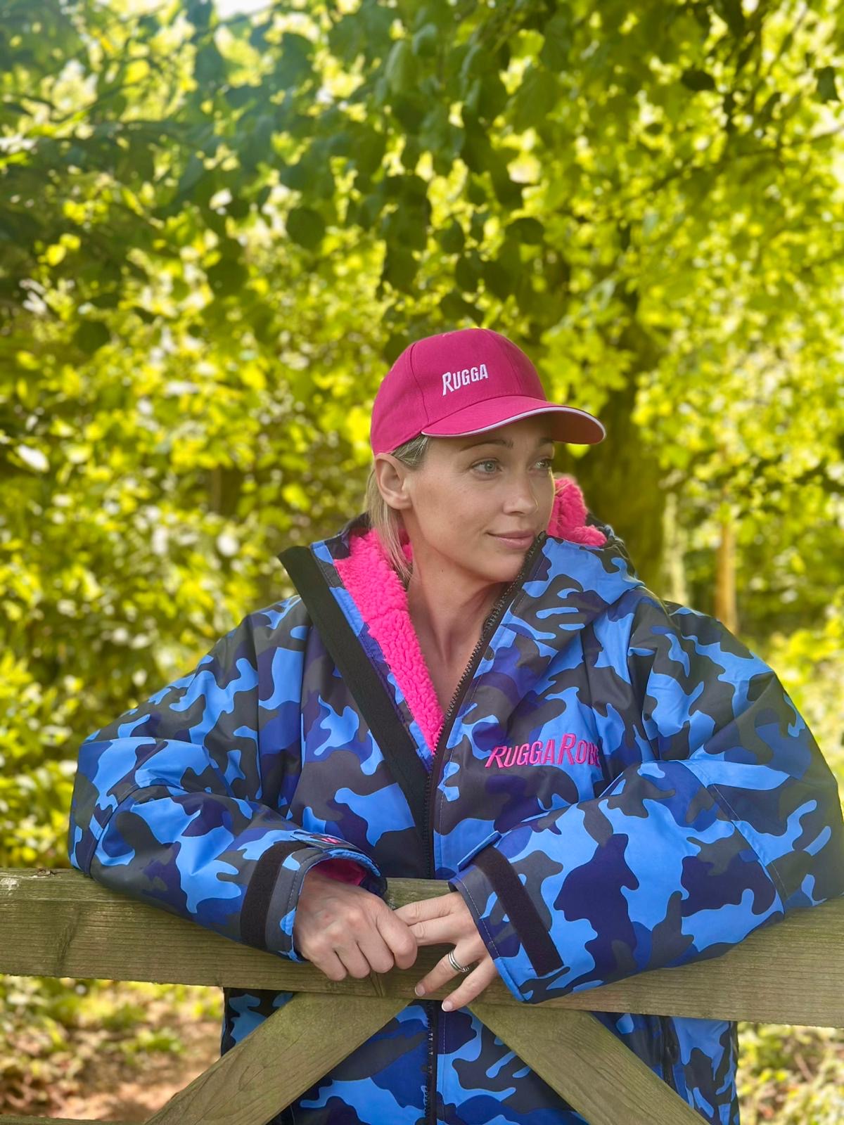 Person wearing a blue camouflage jacket and pink cap with 'ruggarobe' branding, standing outdoors.