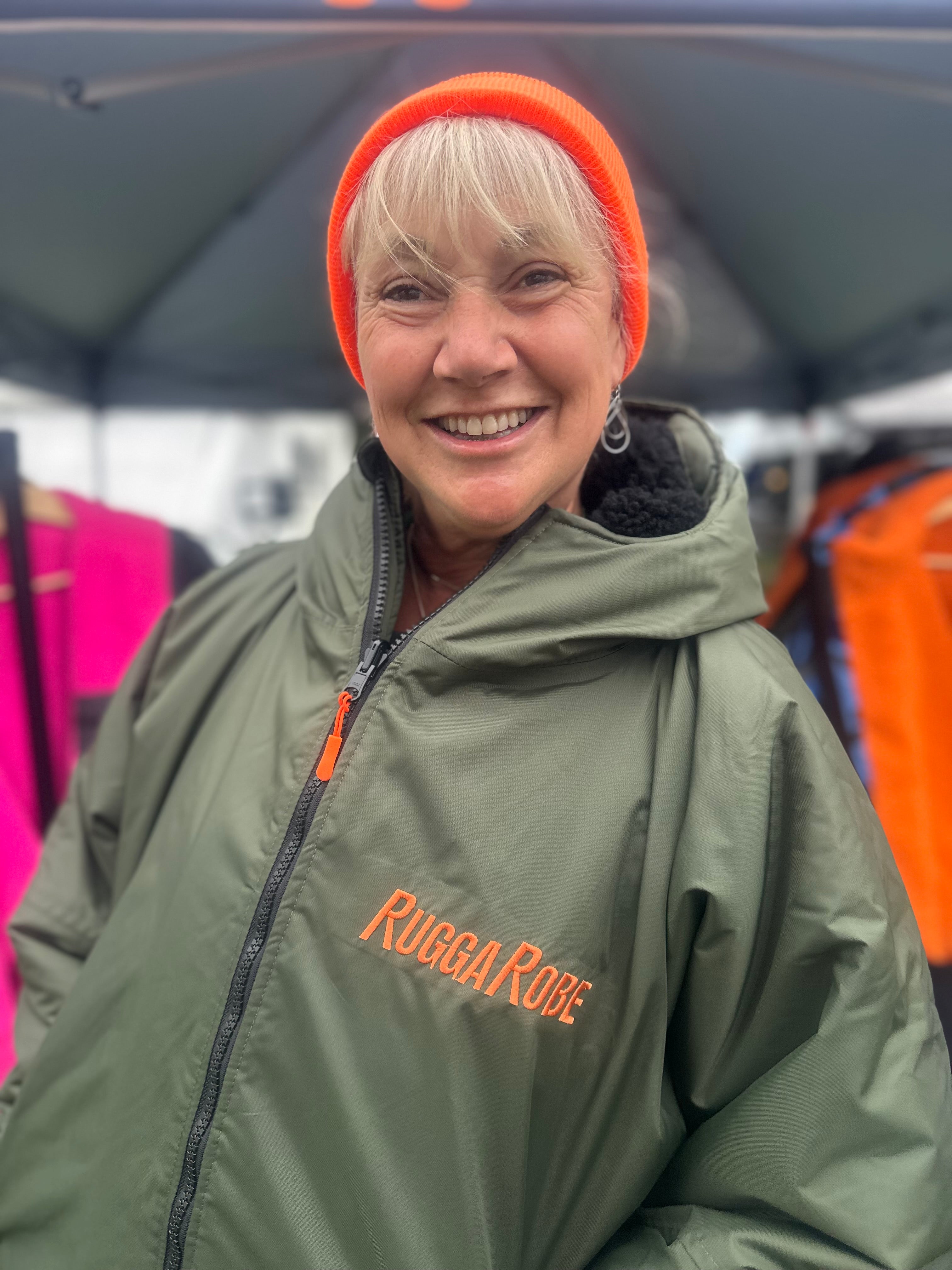 Person wearing a green change robe with 'Rugga Roge' branding, smiling outdoors.