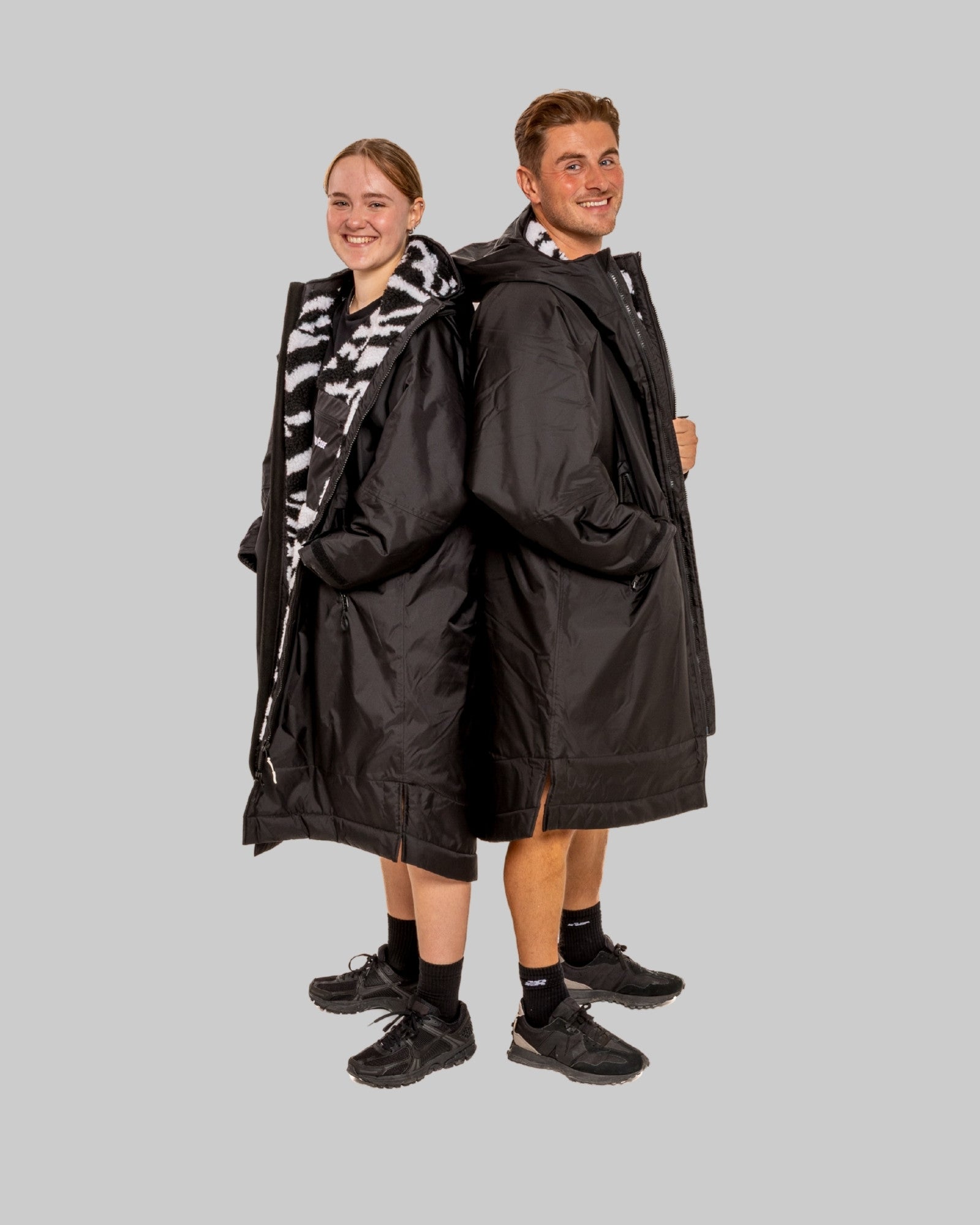 Two people wearing matching black ruhharobes on a gray background