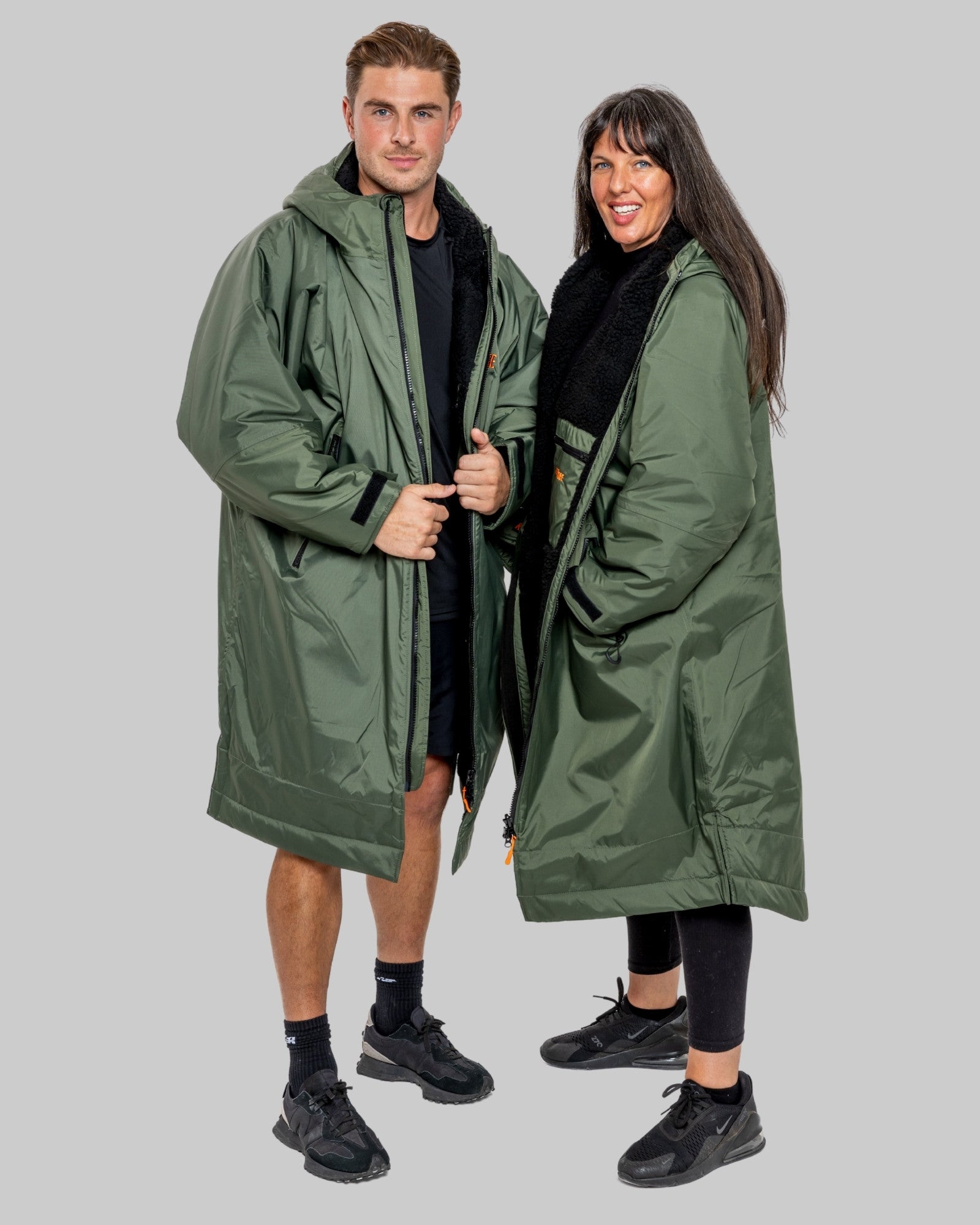 Two people wearing green raincoats on a plain background