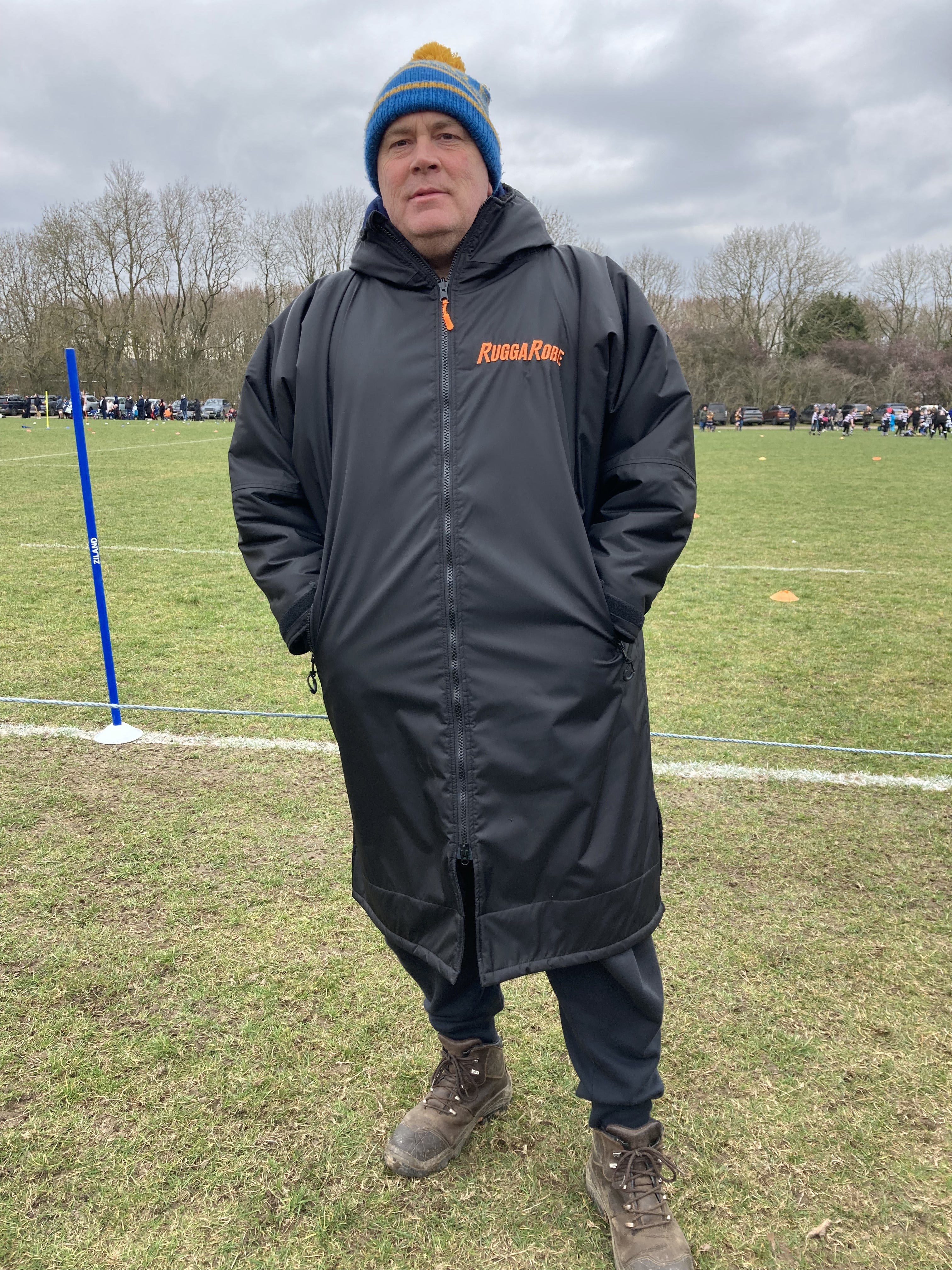 A person wearing a black ruggarobe change robe with black fleece, standing on an outdoor field.