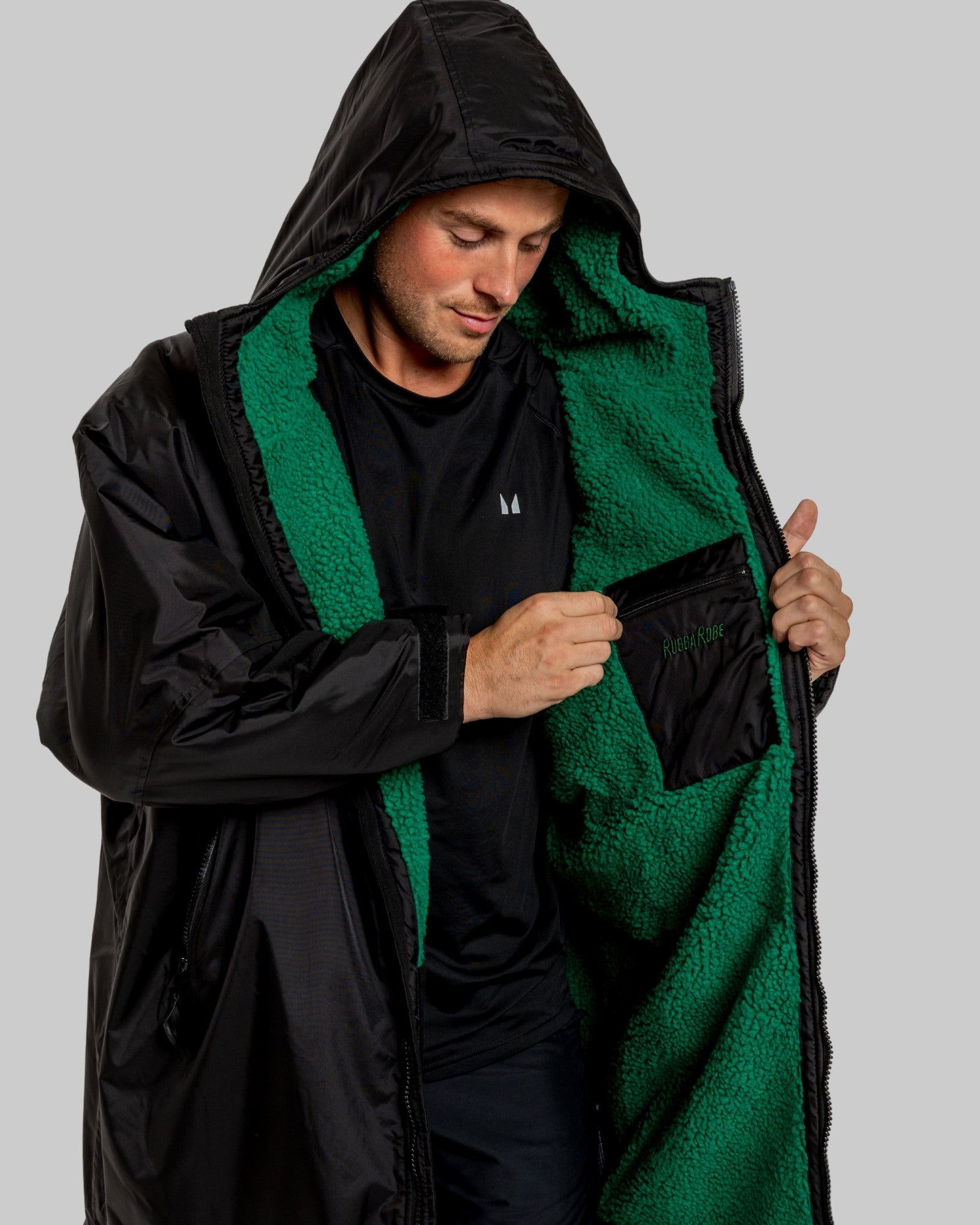 Person wearing a black and green jacket with a hood on a gray background