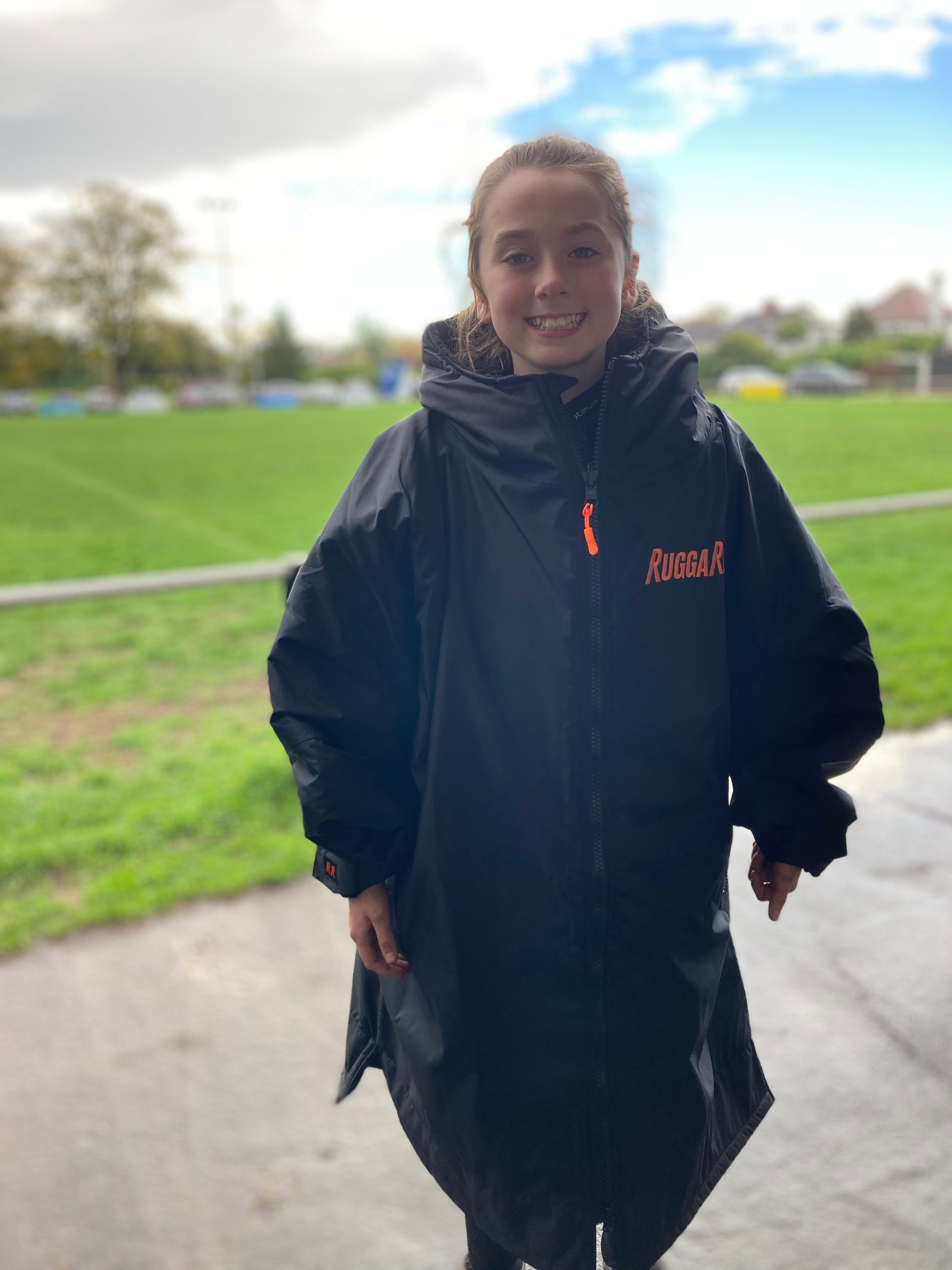 Model wearing RuggaRobe black change robe with orange fleece interior on sports field
