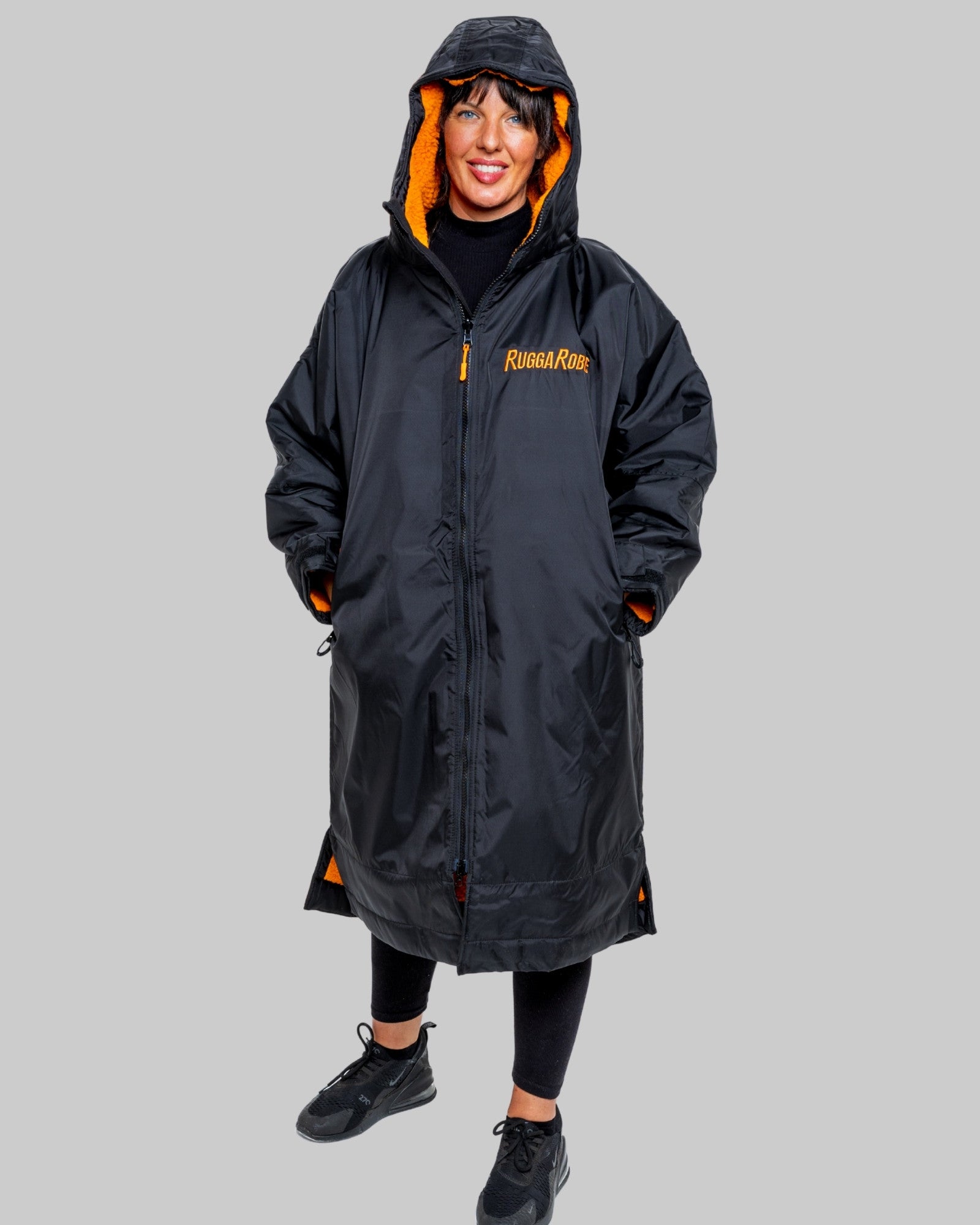 Woman wearing a black changerobe with orange lining and 'RuggaRobe' branding on a grey background