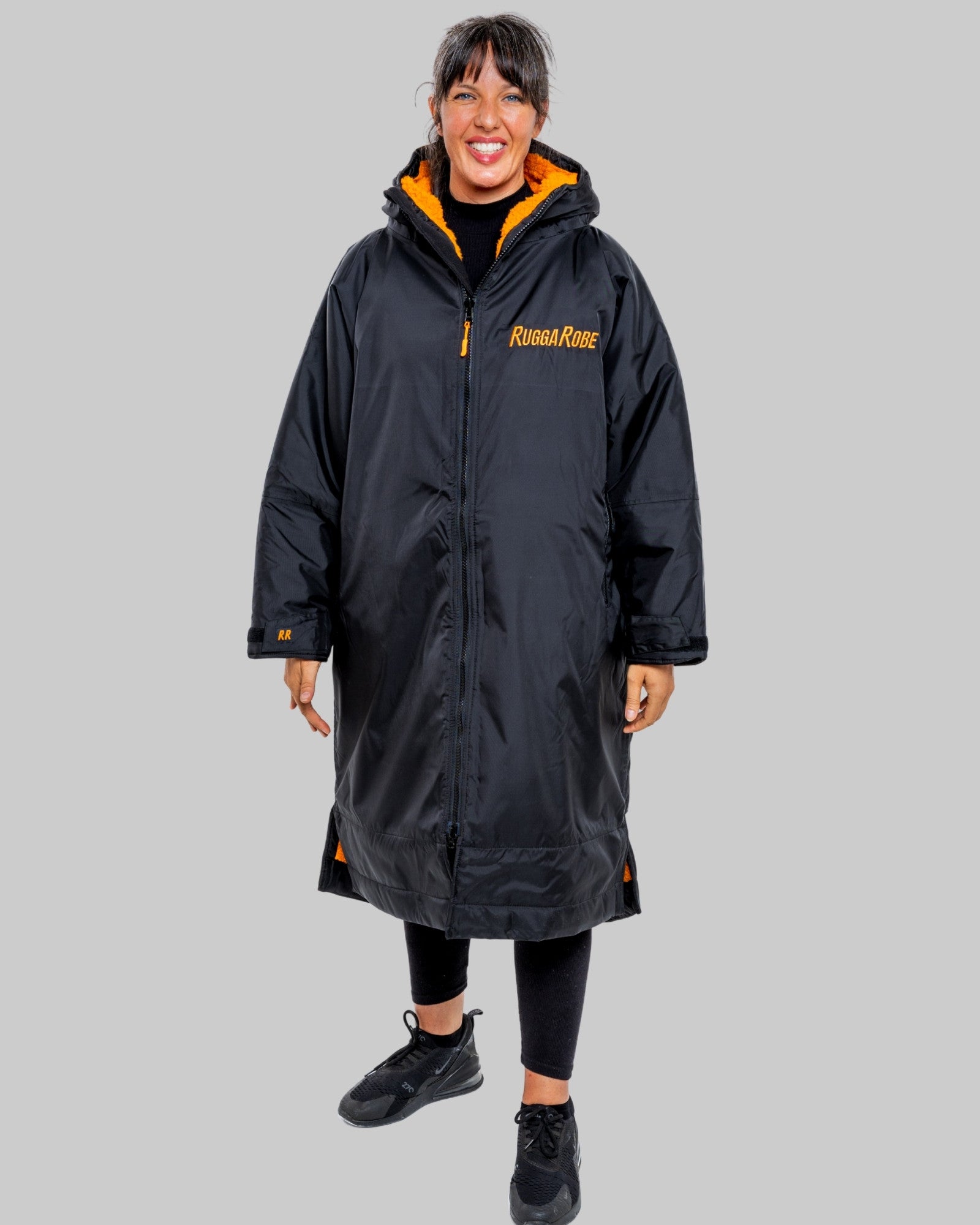 Person wearing a black changerobe with orange interior on a grey background