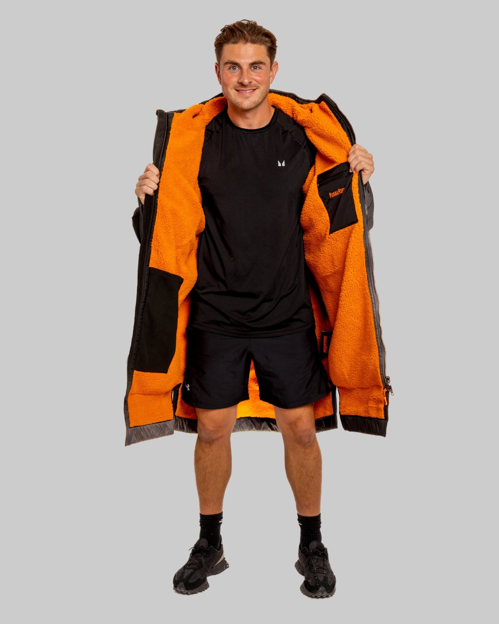 Man wearing a black changerobe with orange lining and 'RuggaRobe' branding on a grey background