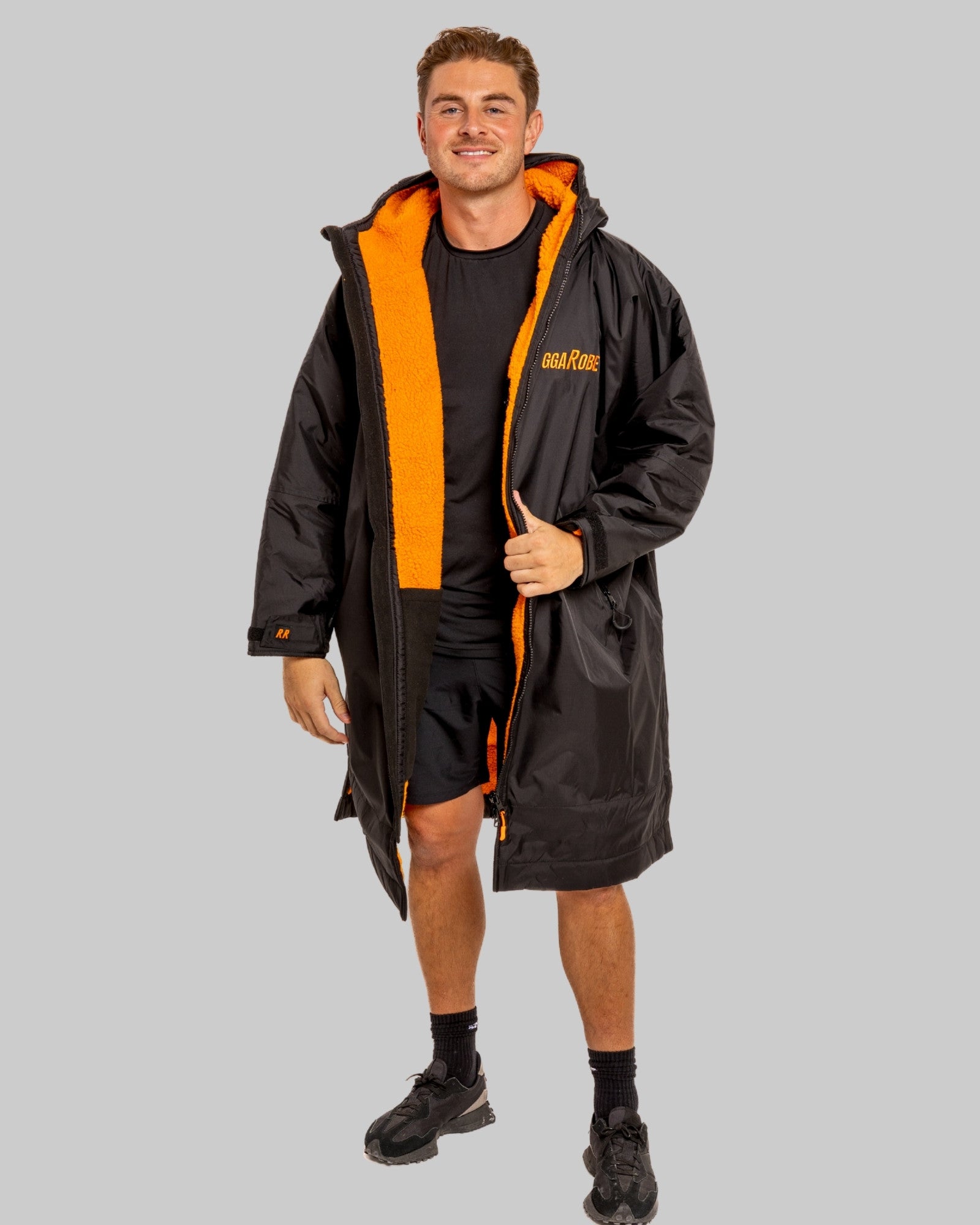 Man wearing a black changerobe with orange lining and 'RuggaRobe' branding on a grey background