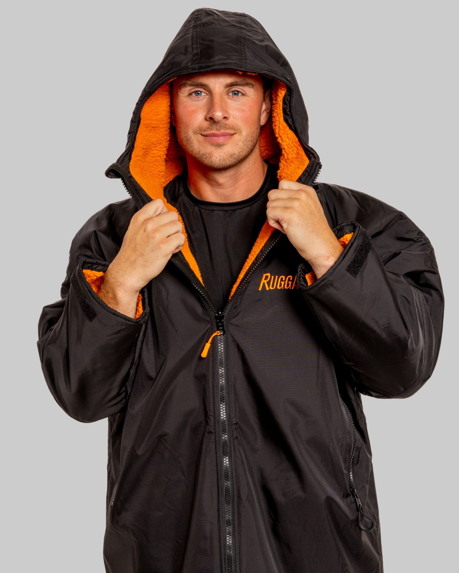 Man wearing a black changerobe with orange lining and 'RuggaRobe' branding on a grey background