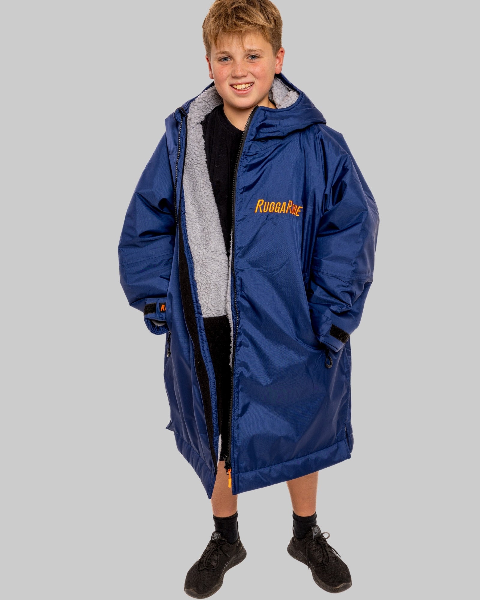 Child wearing a blue RuggaRobe with grey fleece interior change robe on a grey background