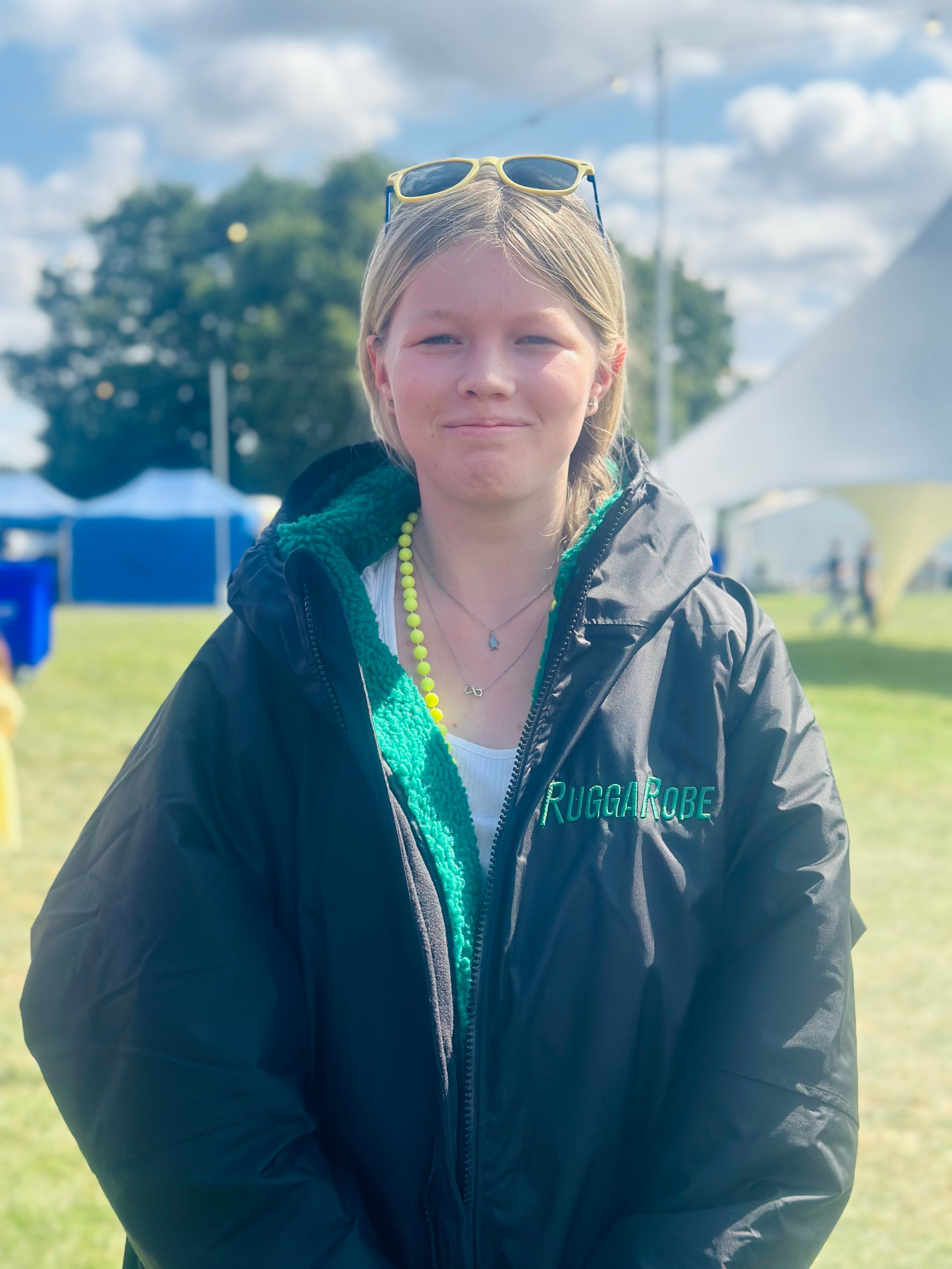 Person wearing a black jacket with 'RuggaRobe' text outdoors on a grassy field.