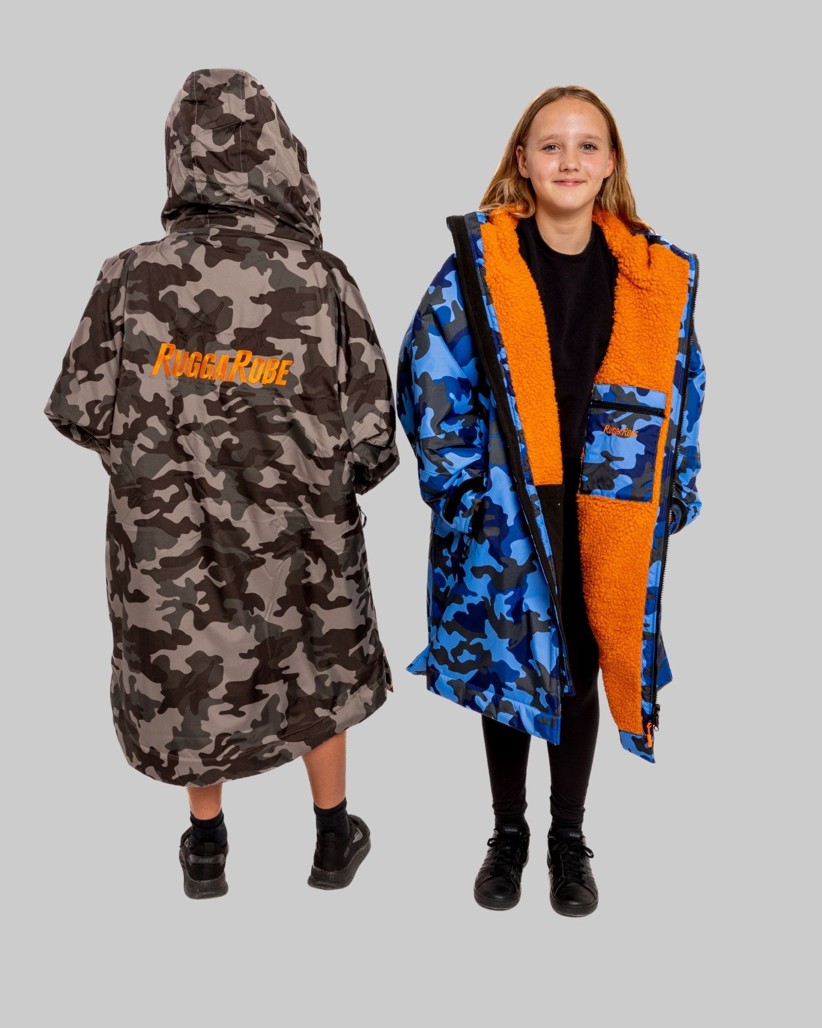 Two children wearing RuggaRobe change robes with camouflage patterns and orange accents on a gray background
