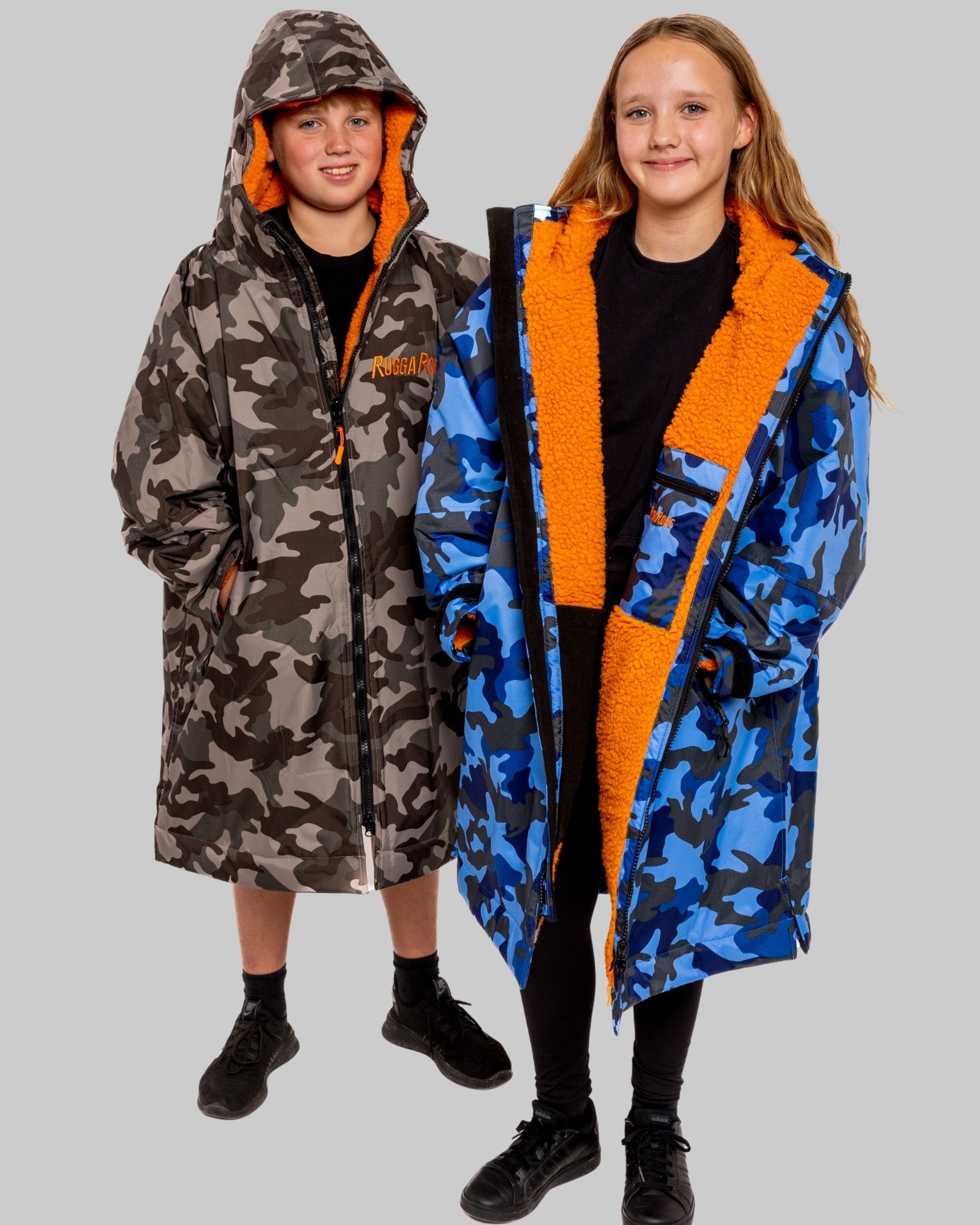 Two children wearing RuggaRobe change robes with camouflage patterns and orange accents on a gray background