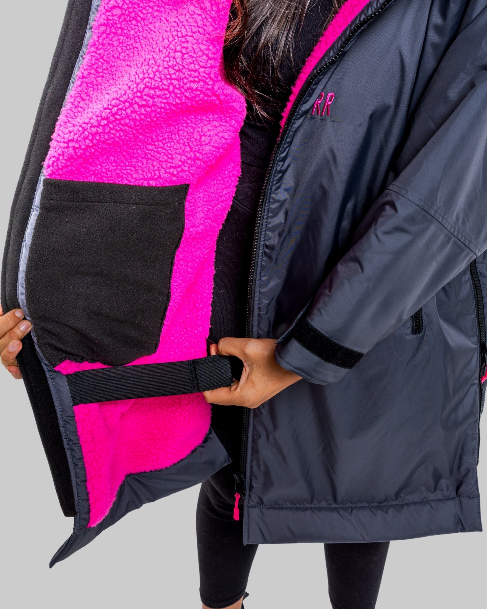 Model wearing a RuggaRobe slate grey change robe with pink fleece interior on a grey background, holding it open to reveal the interior.