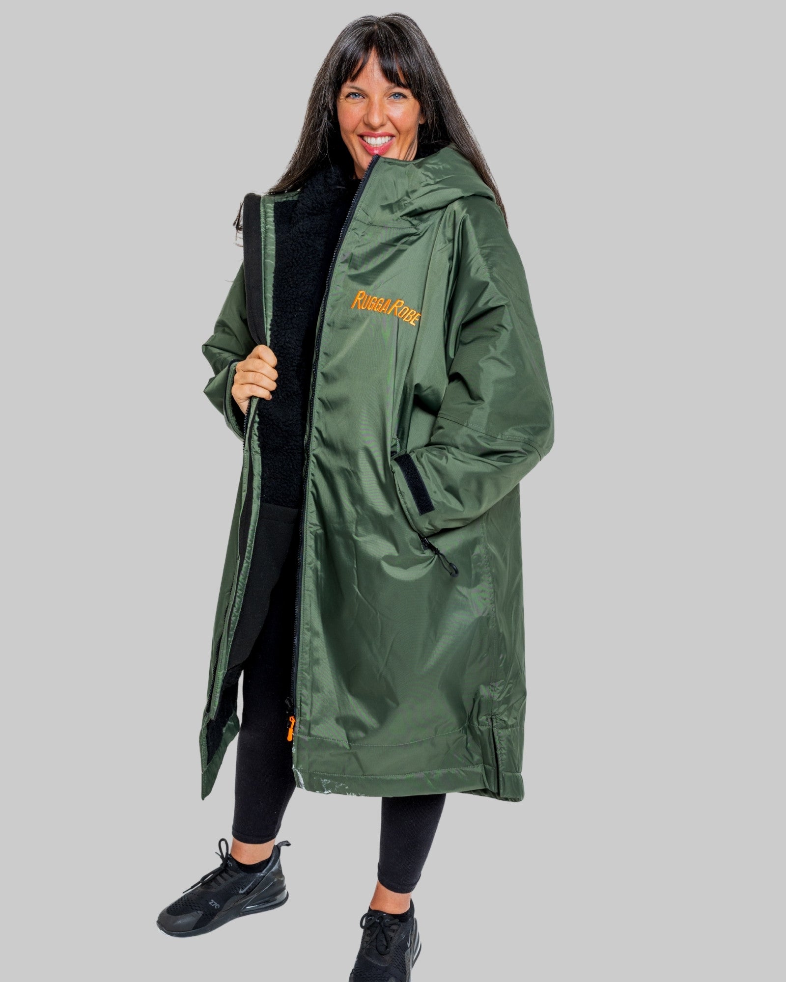 Woman wearing a green change robe with black fleece with a brand logo on a grey background