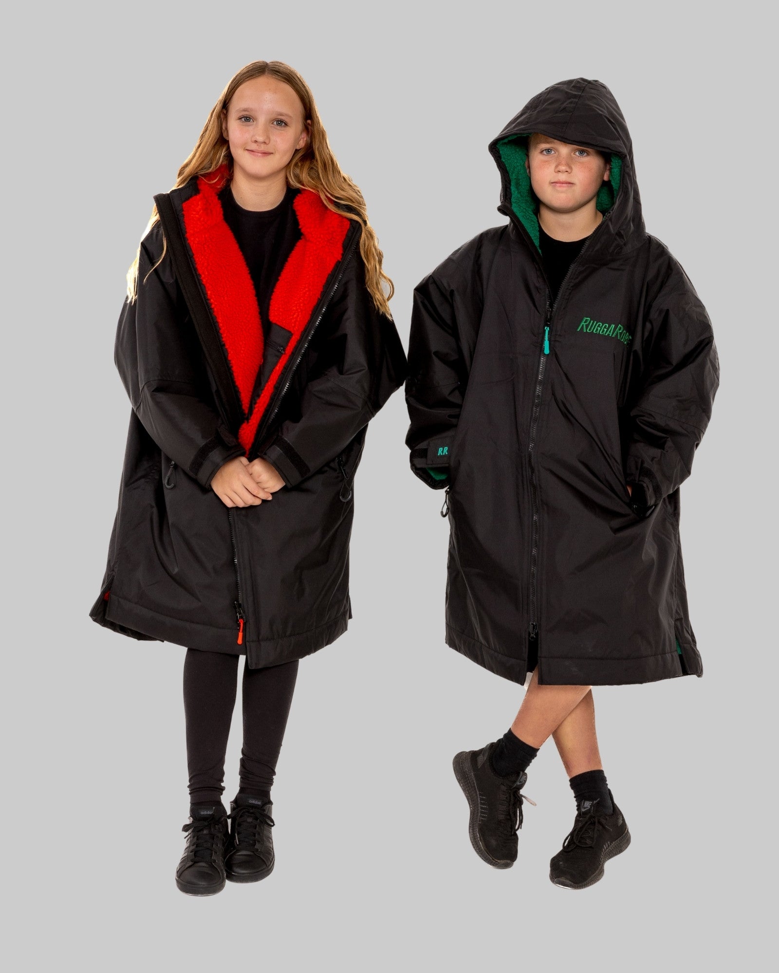Two children wearing black RuggaRobes with red and green accents on a grey background