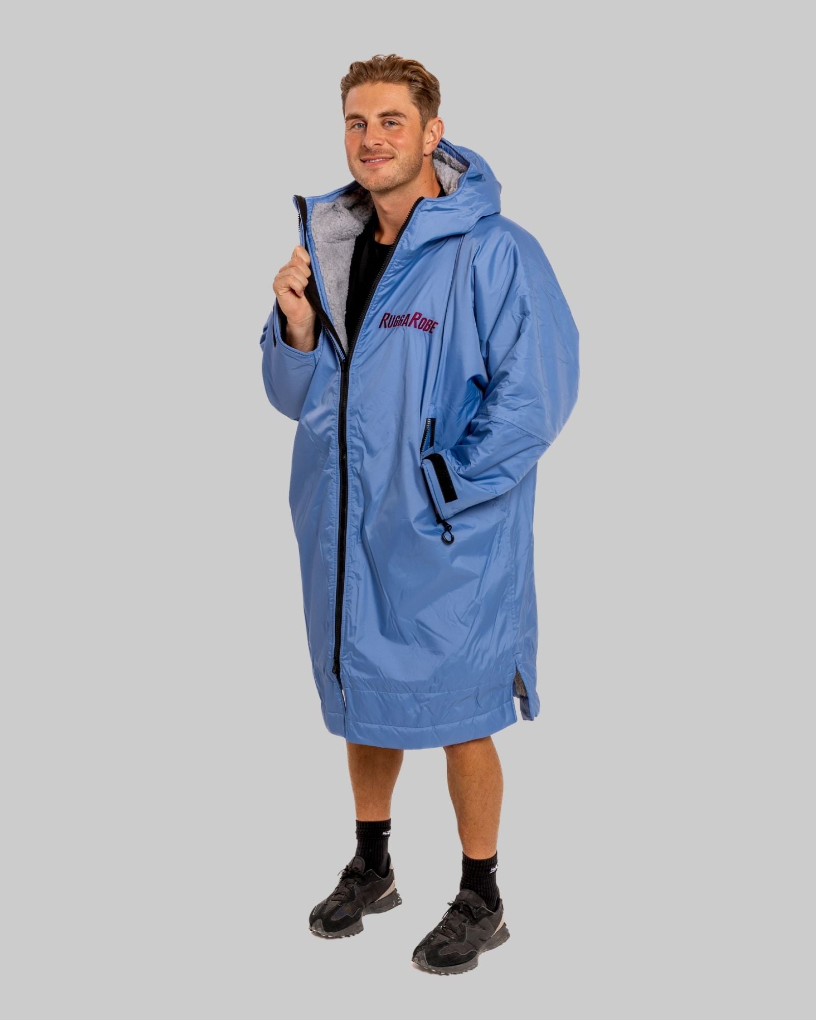 Man wearing a blue raincoat with a ruggarobe brand logo on a gray background