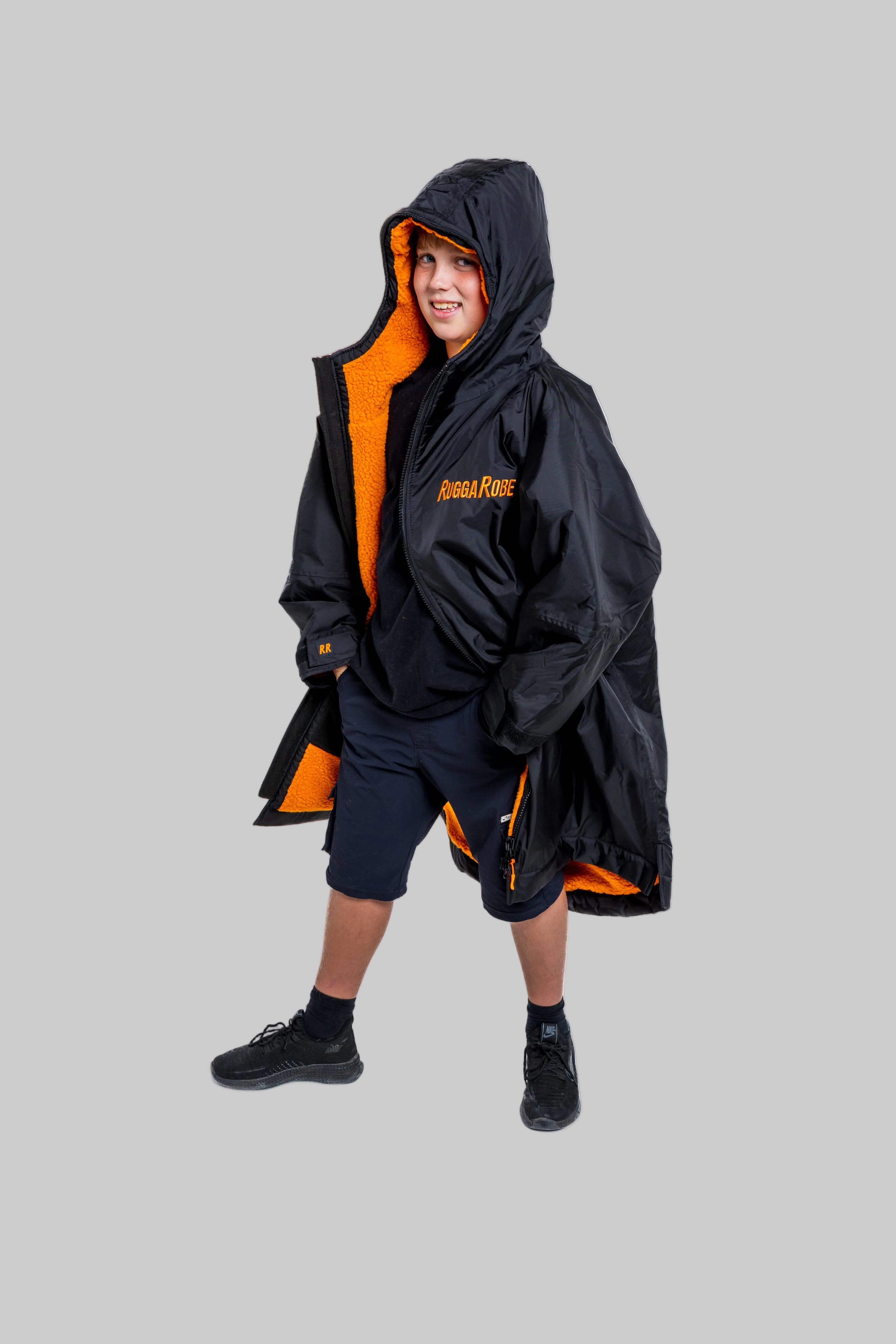 Child wearing RuggaRobe black change robe with orange fleece interior on grey background