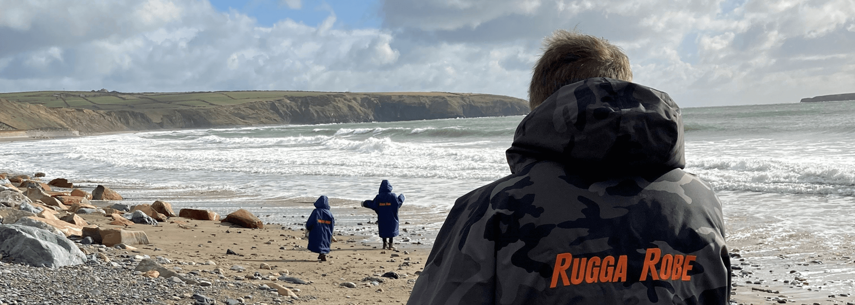 A man on the beach is watching 2 children walking in front of him. Wearing a ruggarobe changerobe