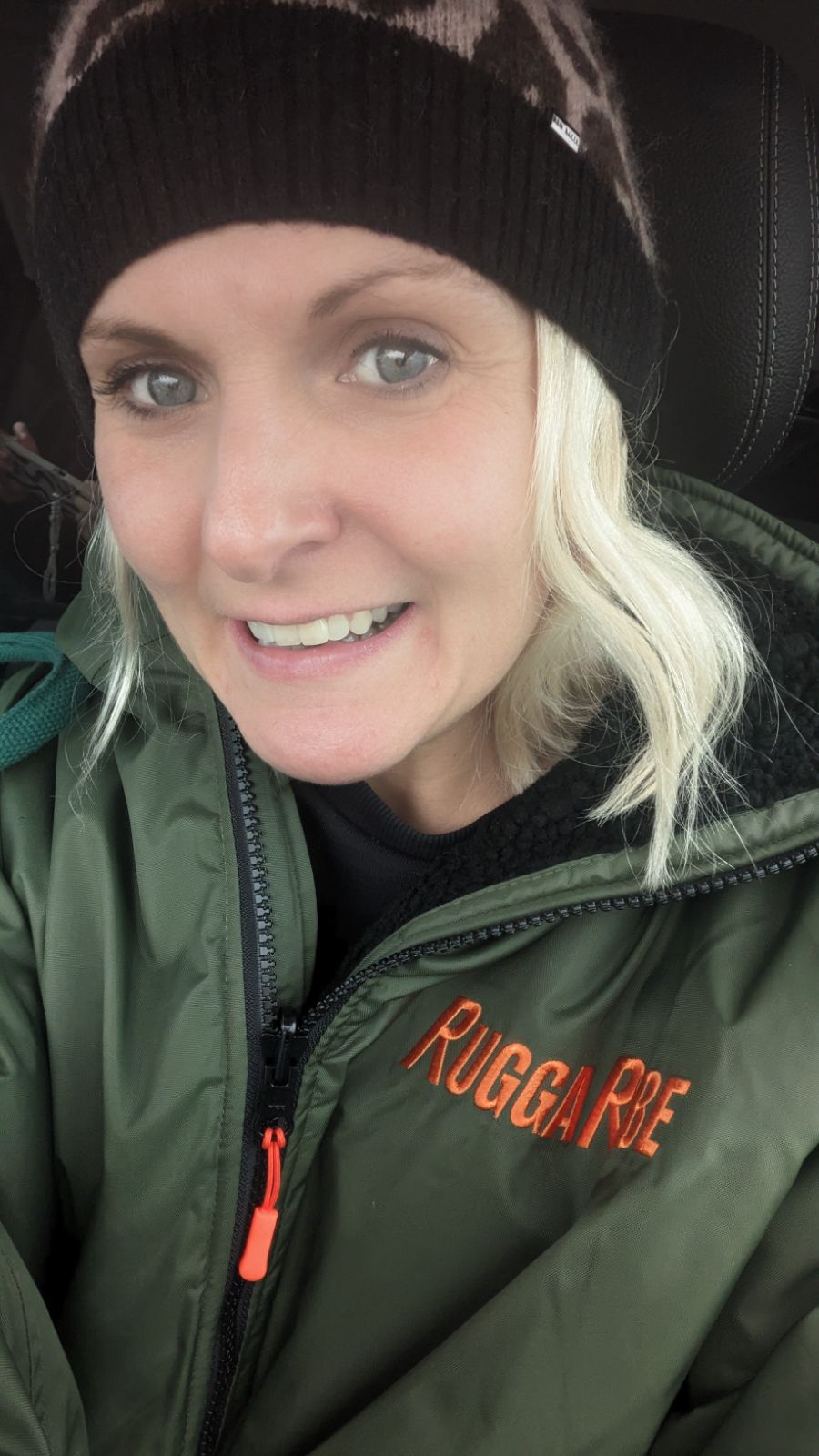 Person wearing a green jacket with 'Ruggrobe' branding inside a vehicle.