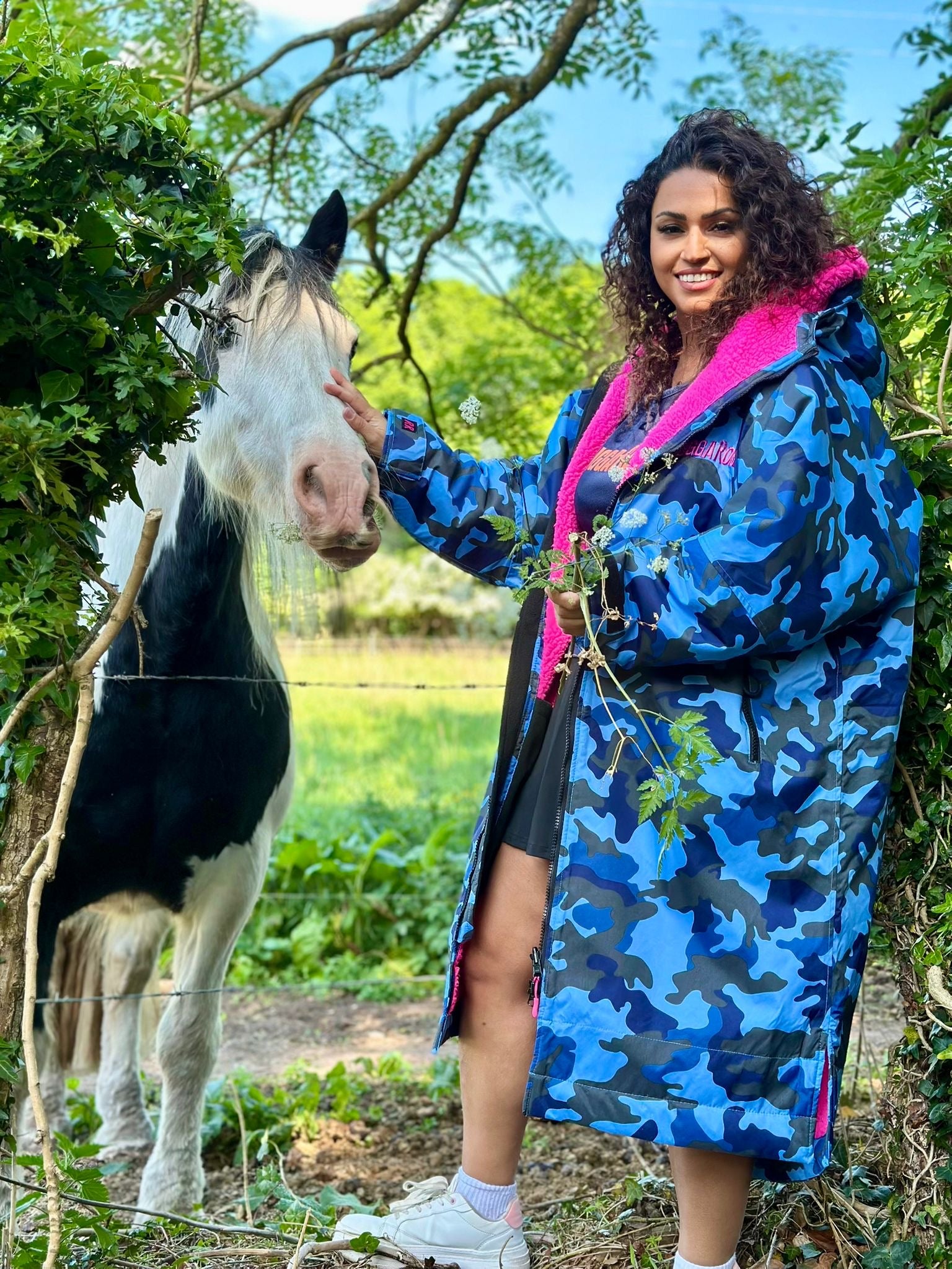 Woman in a blue camouflage ruggarobe petting a horse in a natural setting