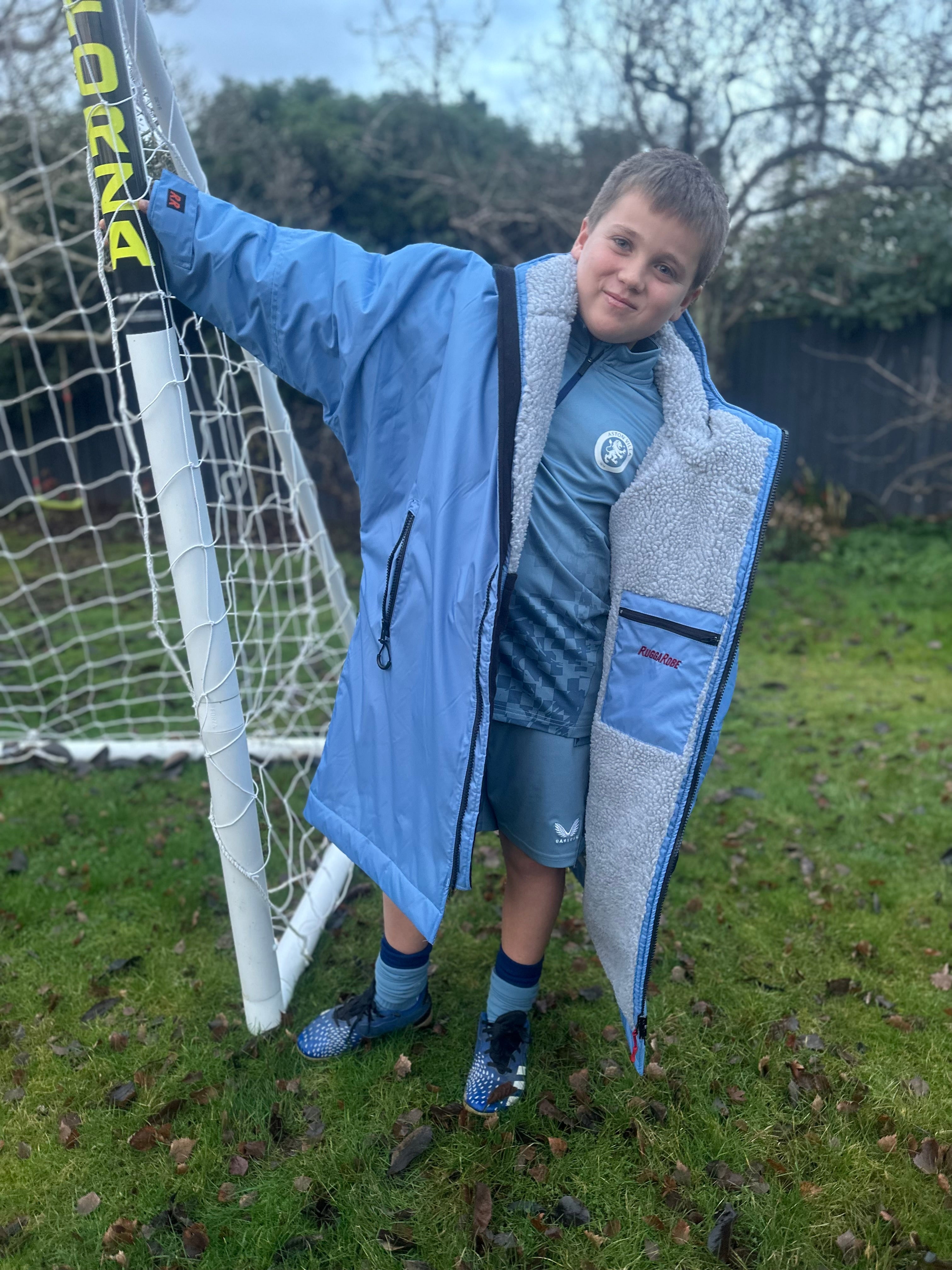 Child in blue changerobe and shorts standing in front of a soccer goal