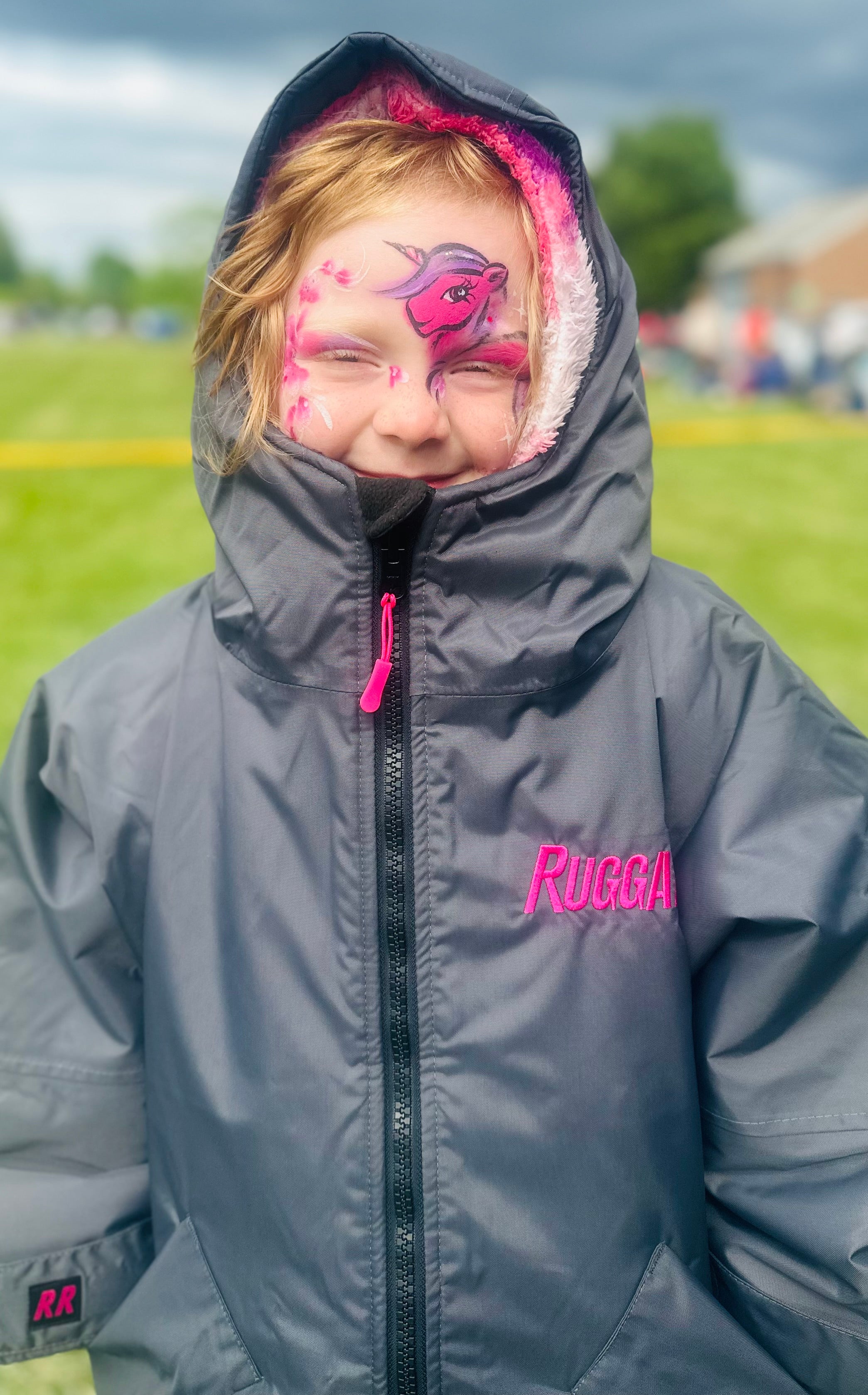 Child wearing RuggaRobe slate grey change robe with pink fleece interior on a grassy field