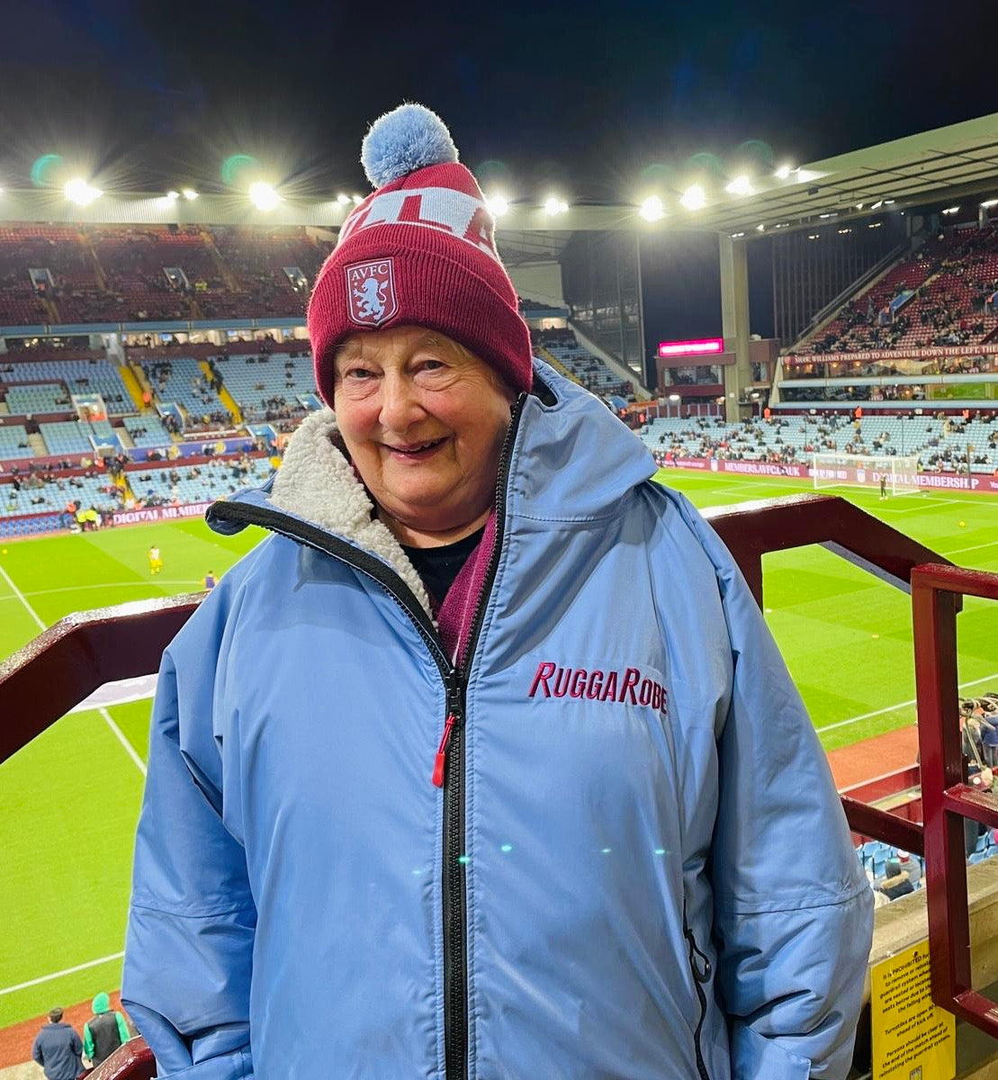 Person wearing a blue jacket and red beanie with a logo at a sports stadium.