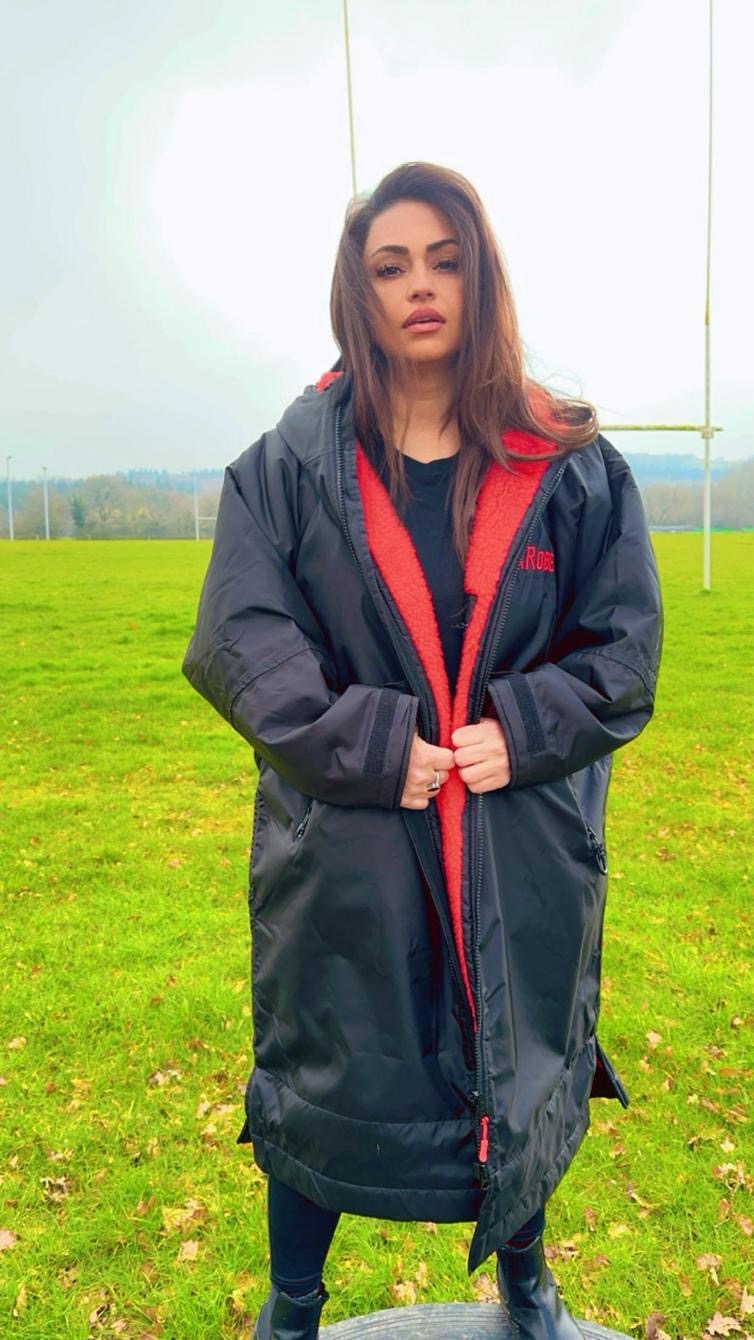 Model wearing RuggaRobe black change robe with red fleece interior in a sportsfield