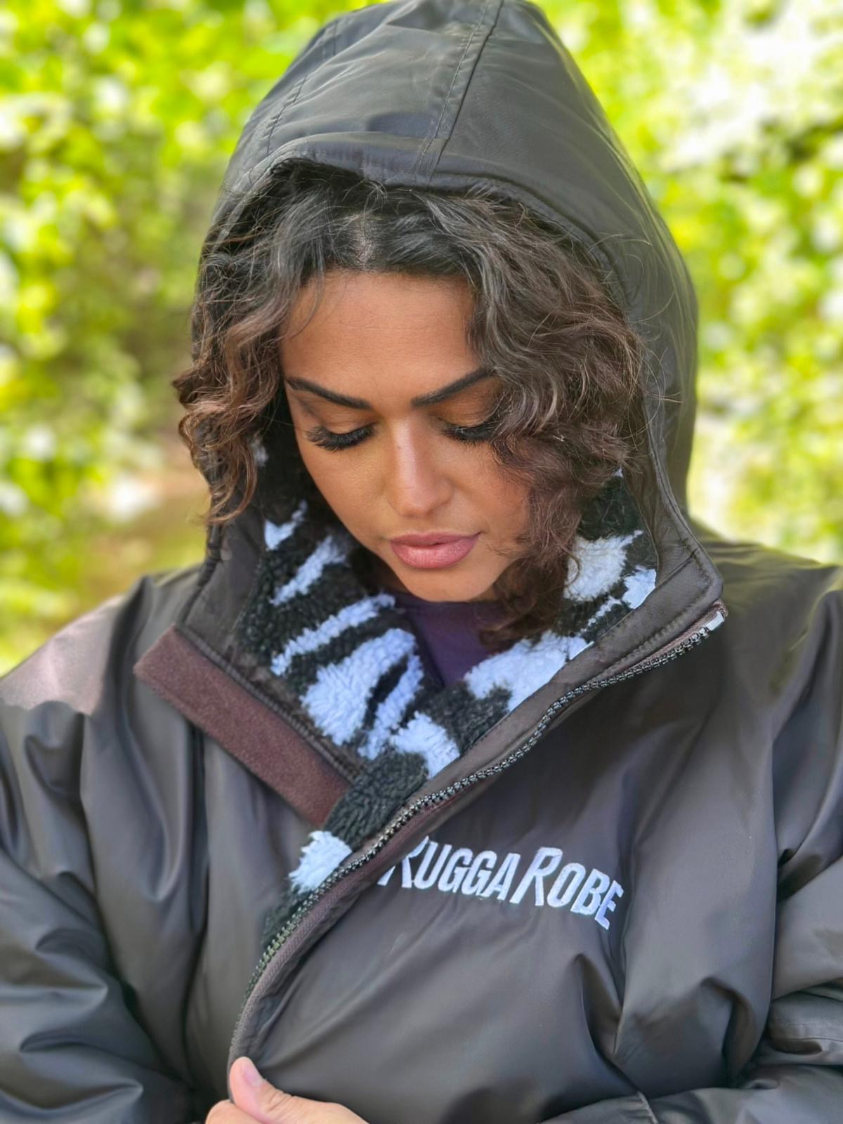Person wearing a black hooded jacket with a ruggarobe logo, sitting outdoors.