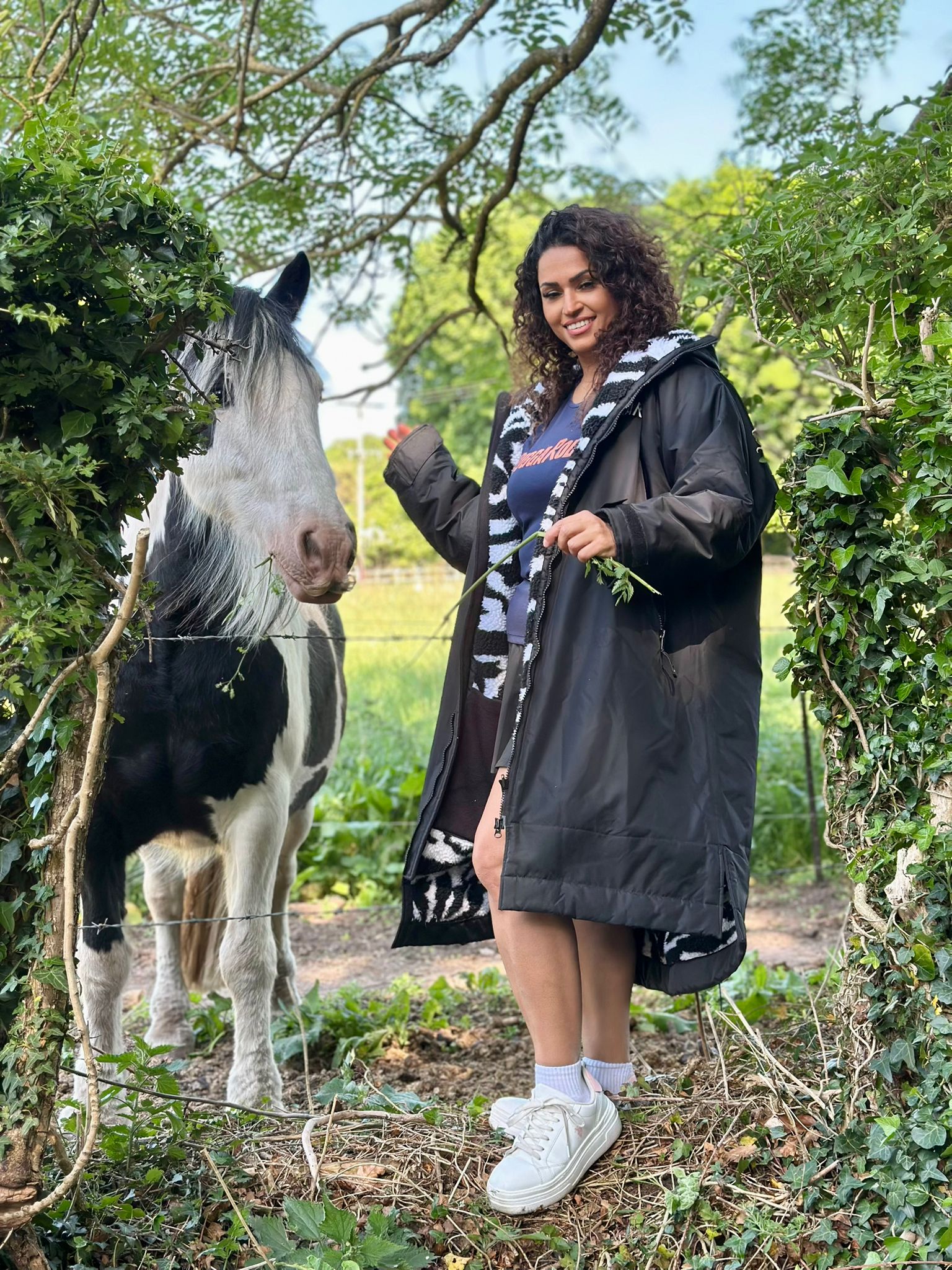 Woman standing next to a horse in a natural setting wearing a black changerobe