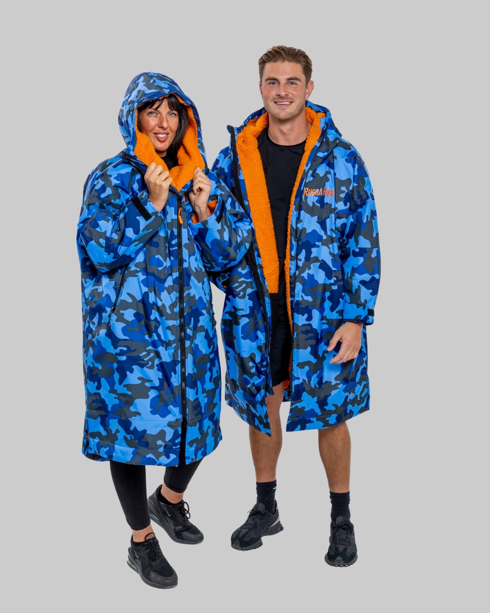 Two people wearing blue camouflage changerobes with orange fleece lining on a grey background