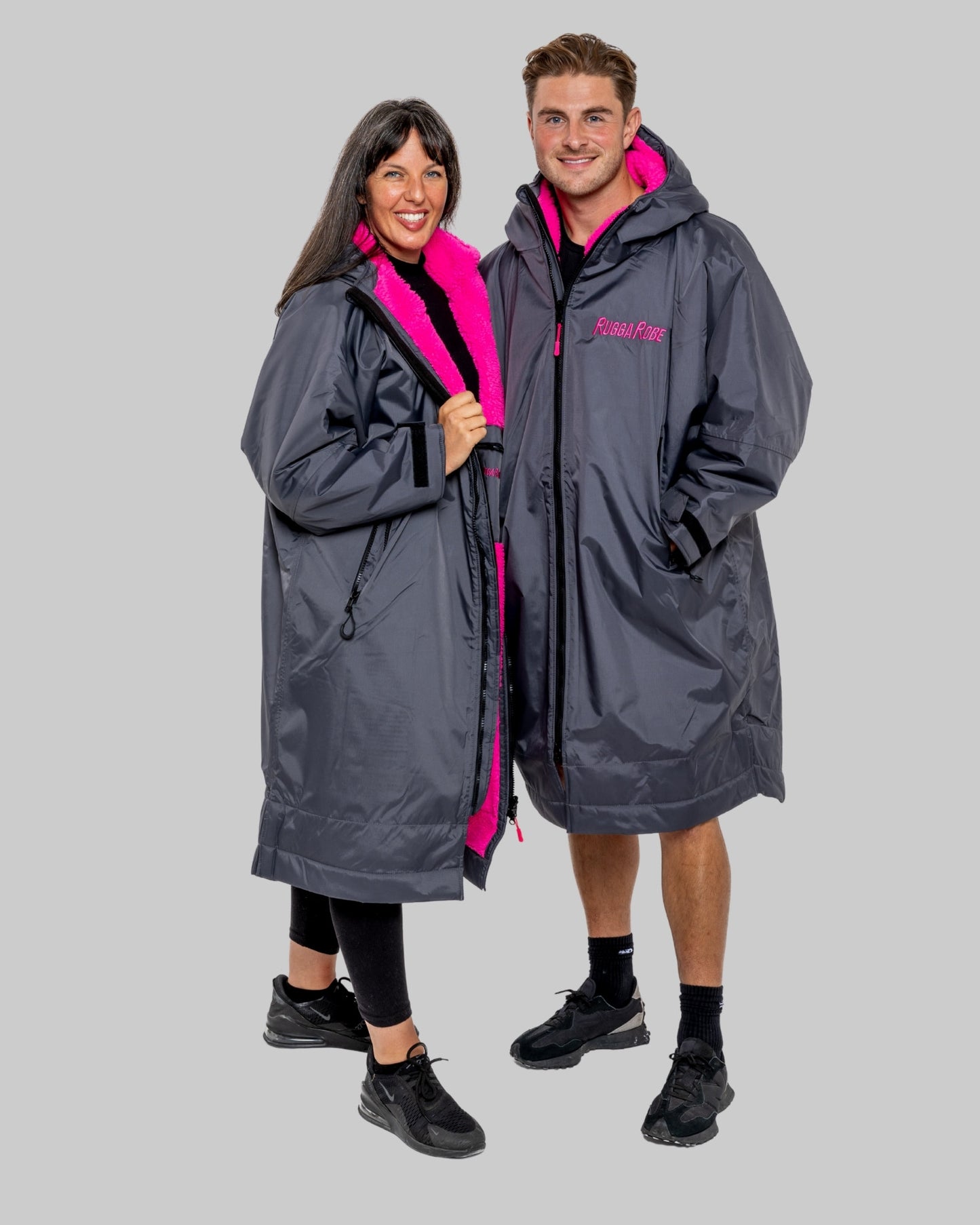 Two models wearing RuggaRobe slate grey change robe with pink fleece interior on a grey background