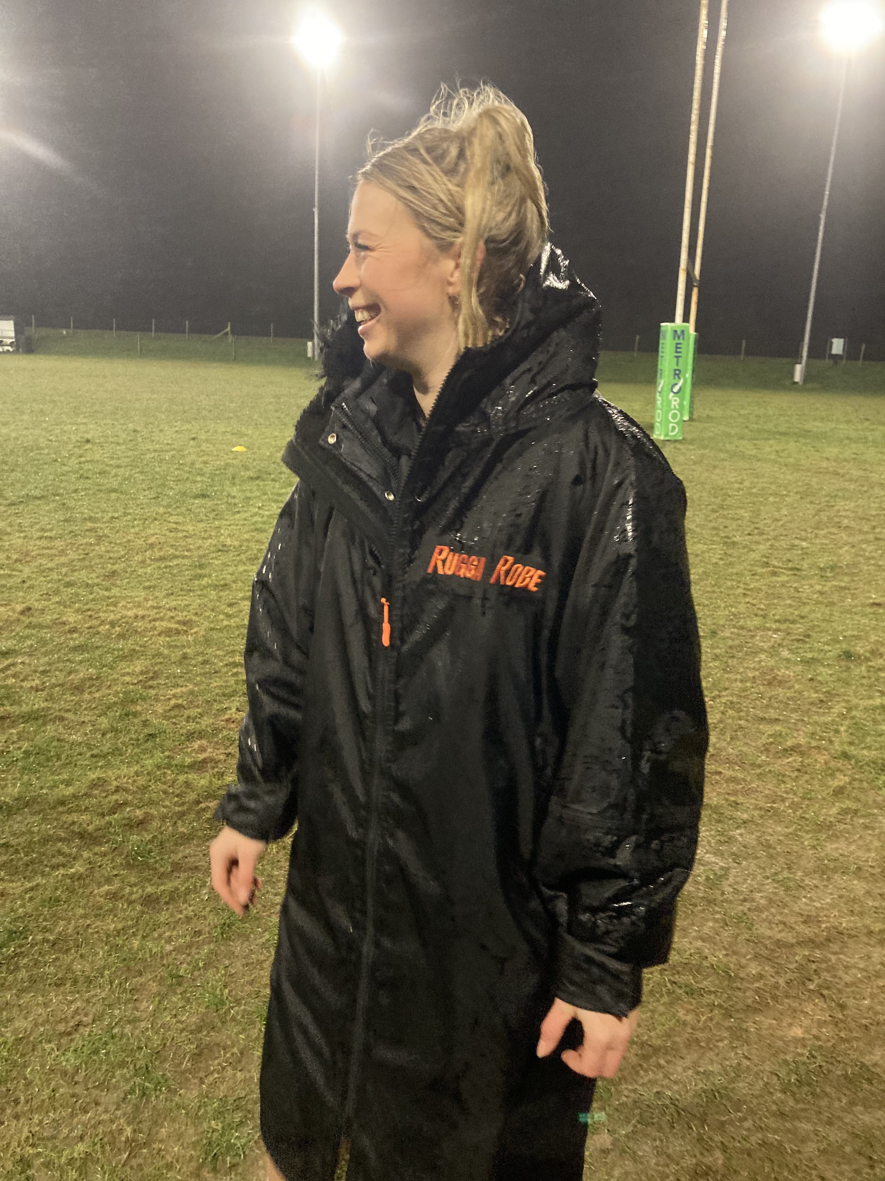 A person wearing a black ruggarobe change robe with black fleece, standing on an outdoor field.