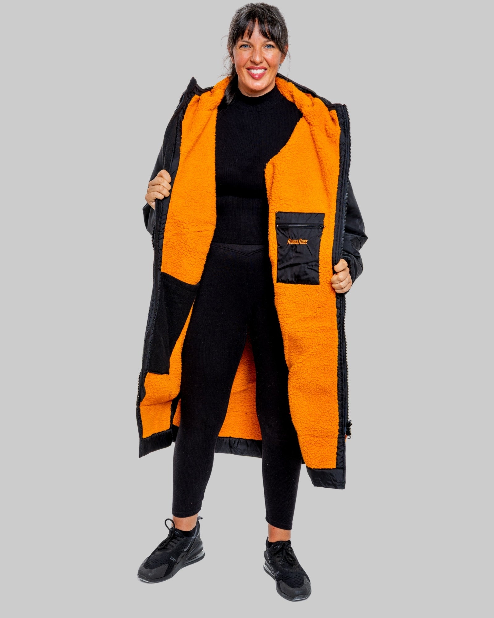 Woman wearing a black changerobe with orange lining and 'RuggaRobe' branding on a grey background
