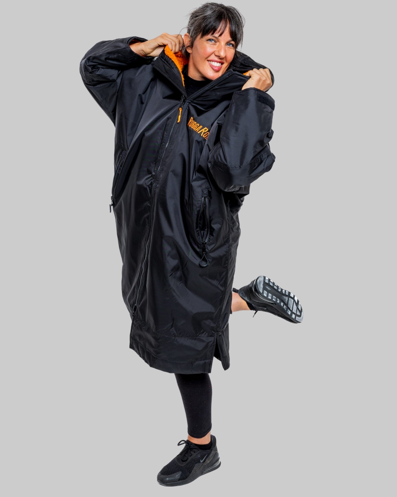 Woman wearing a black changerobe with orange lining and 'RuggaRobe' branding on a grey background