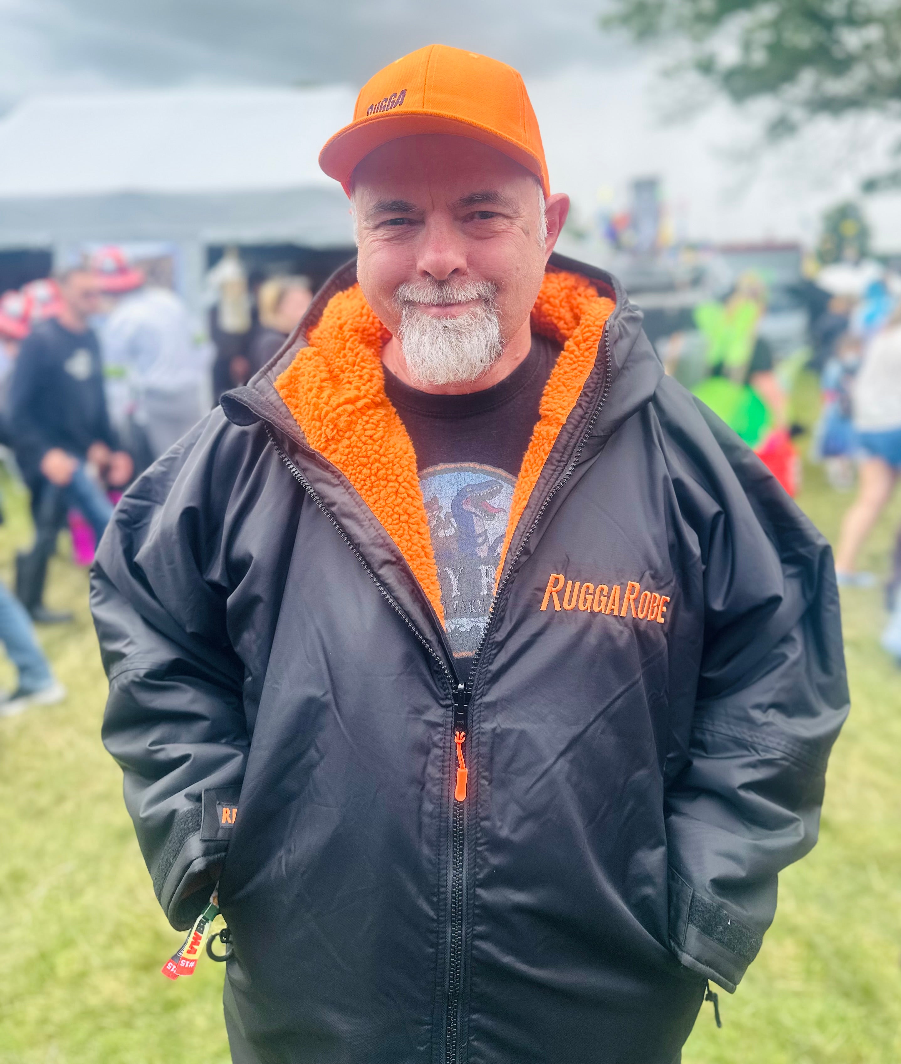 Man wearing an orange cap and black ruggarobe with orange lining, standing outdoors with a crowd in the background.