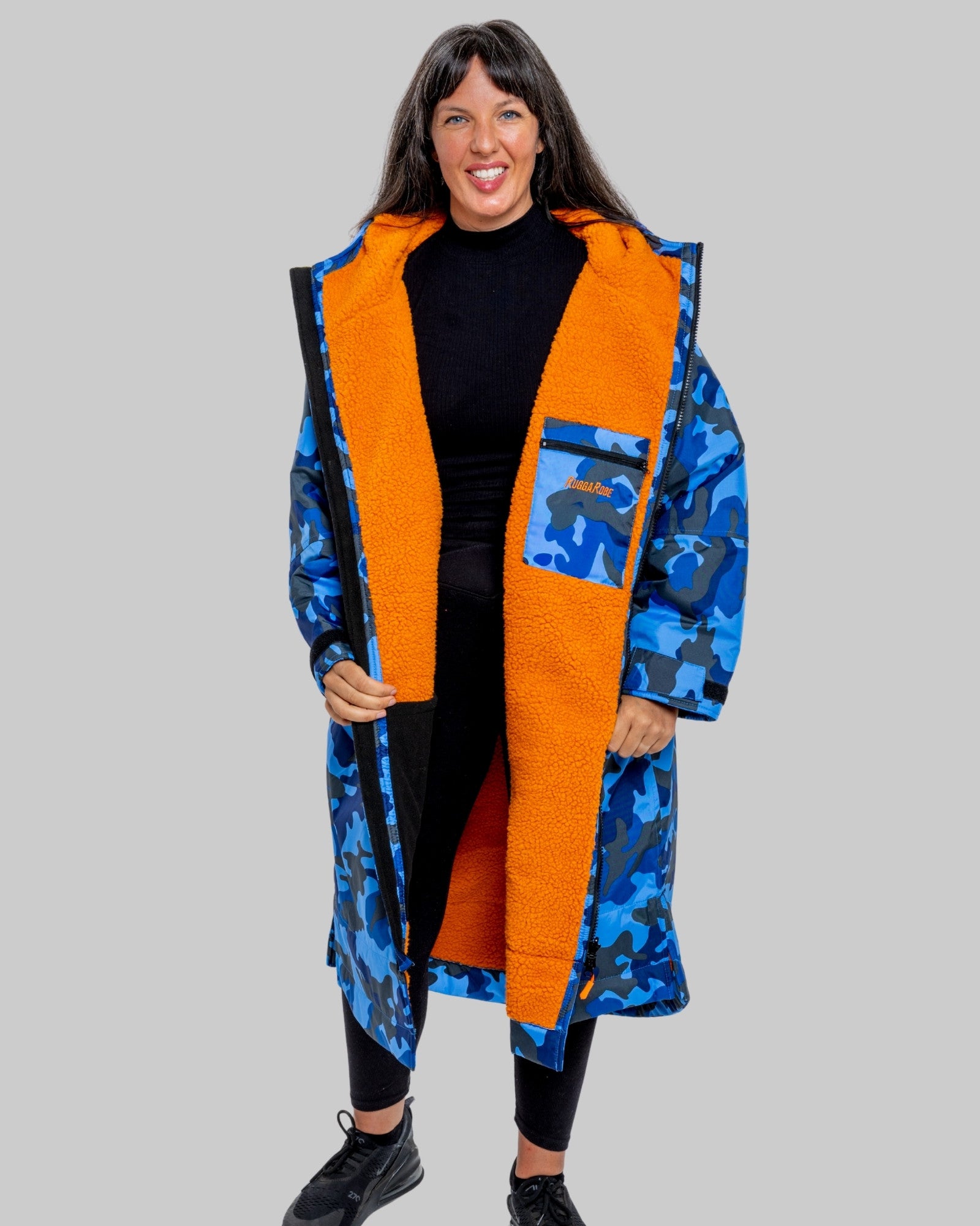 Woman wearing a blue camo changerobe with orange lining and 'RuggaRobe' branding on a grey background