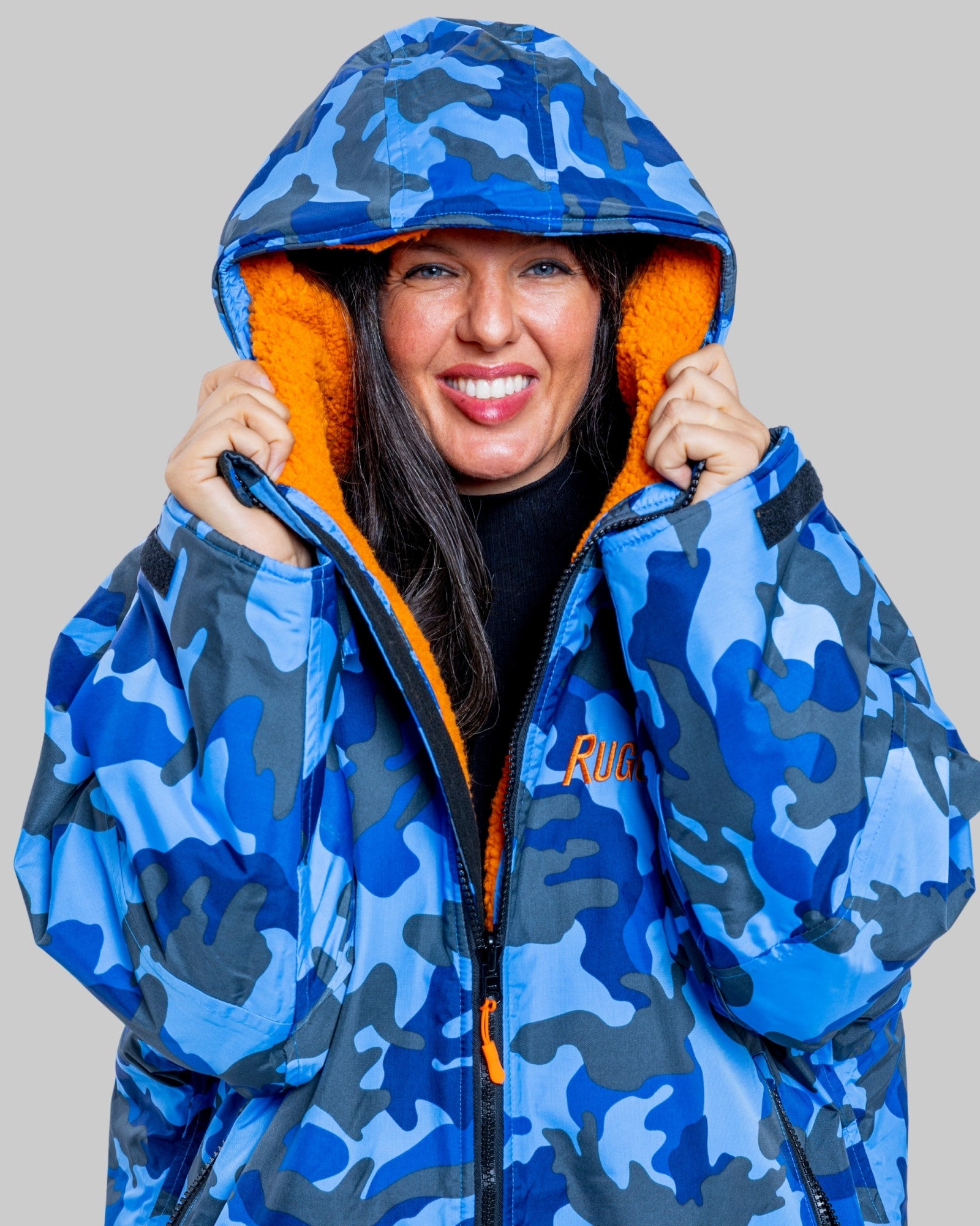 Woman wearing a blue camo changerobe with orange lining and 'RuggaRobe' branding on a grey background