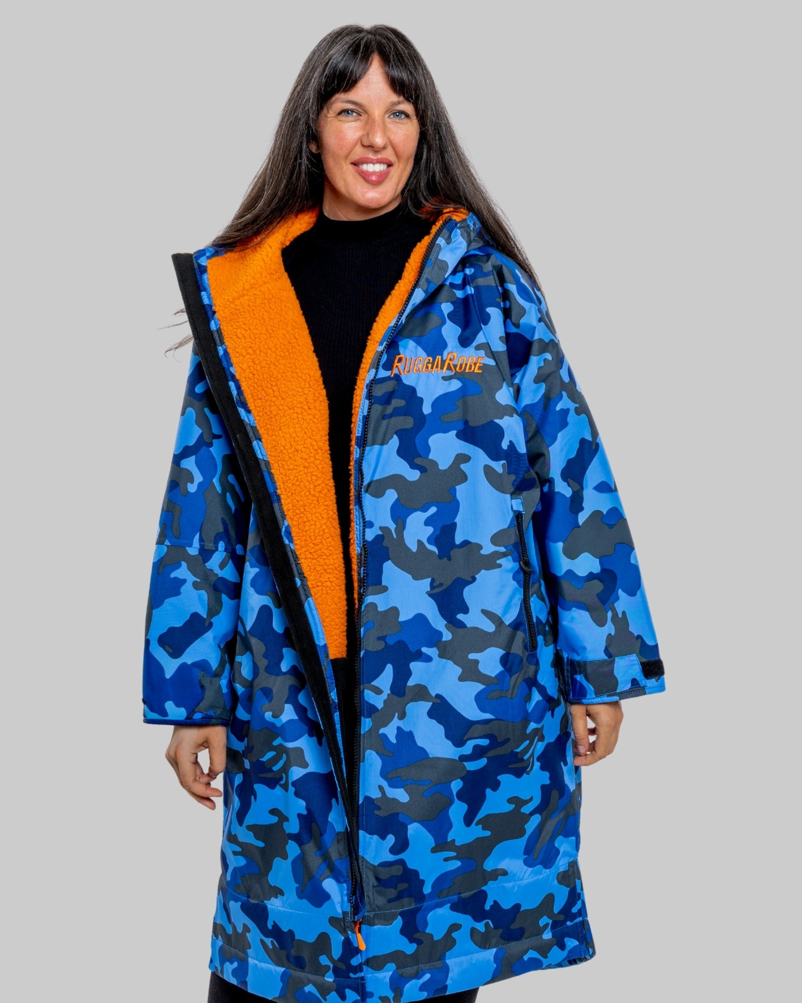Woman wearing a blue camo changerobe with orange lining and 'RuggaRobe' branding on a grey background