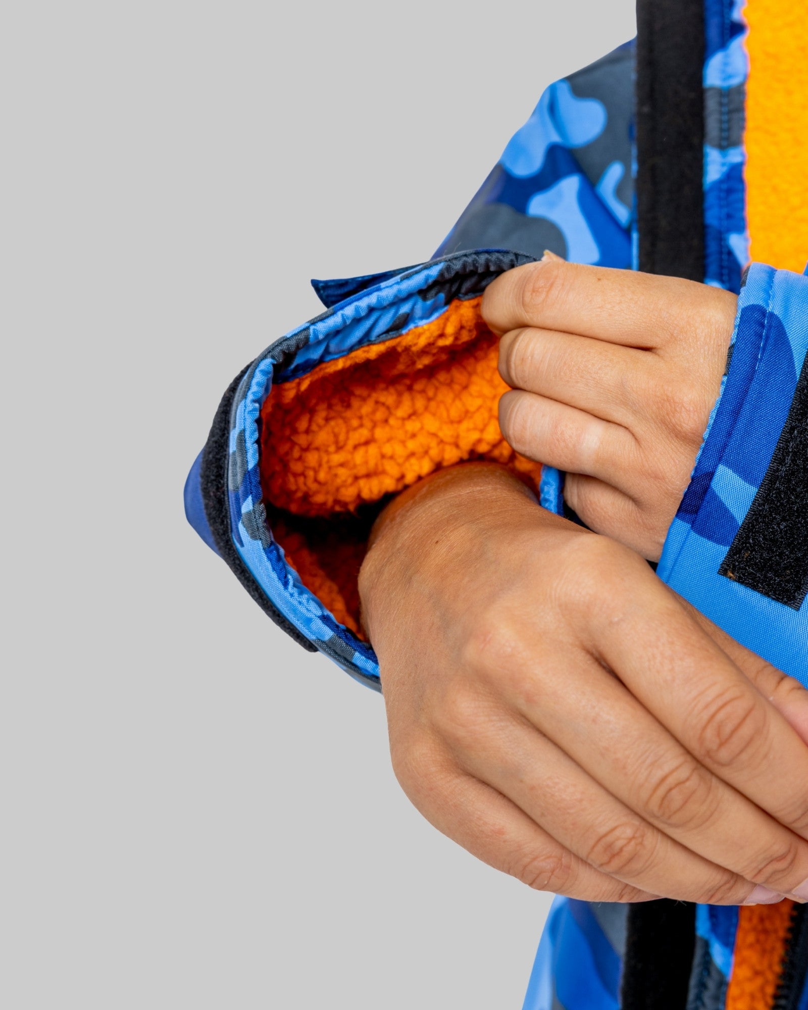 Hand adjusting a blue camo and orange RuggaRobet on a grey background