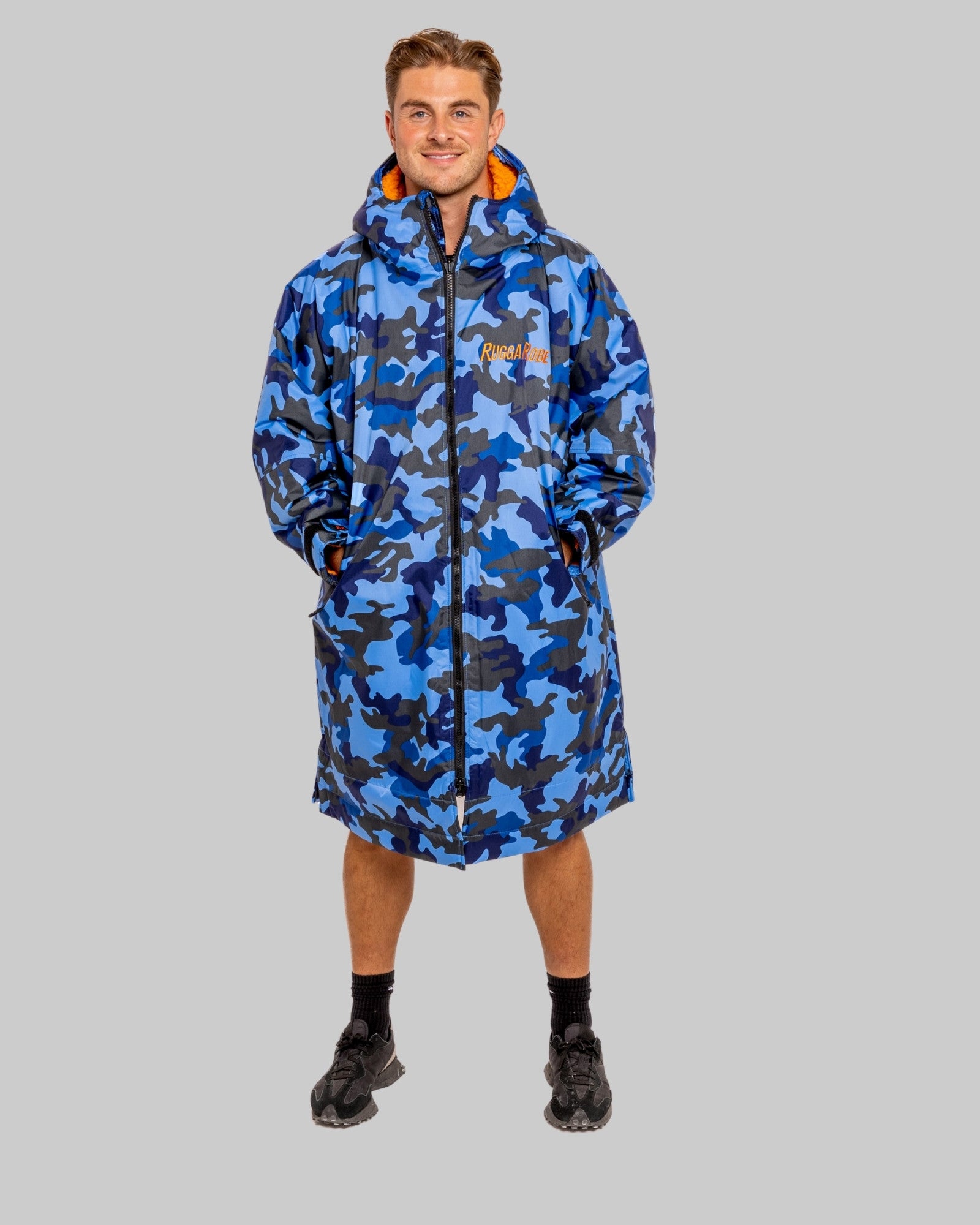 Man wearing a blue camo changerobe with orange lining and 'RuggaRobe' branding on a grey background