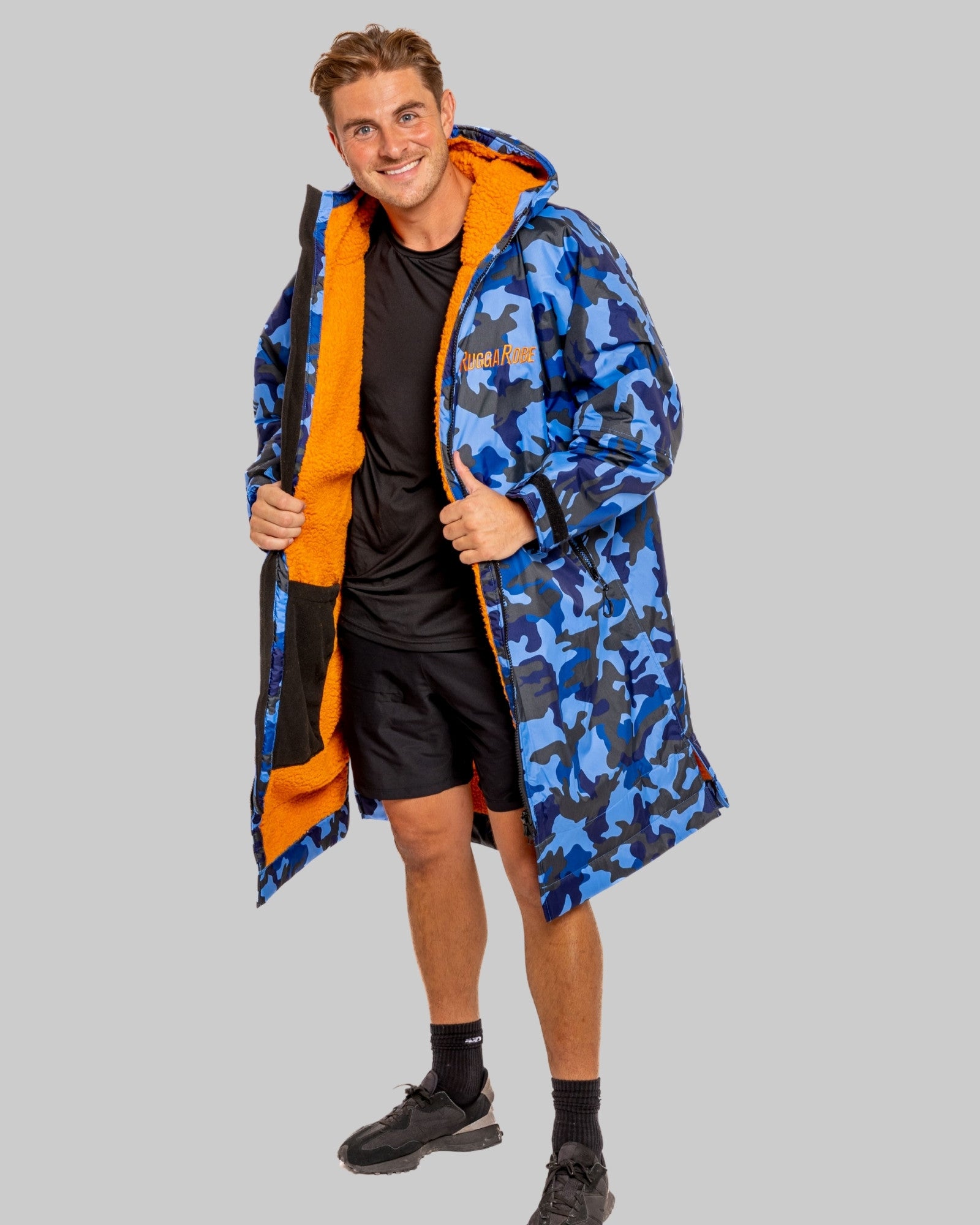 Man wearing a blue camo changerobe with orange lining and 'RuggaRobe' branding on a grey background