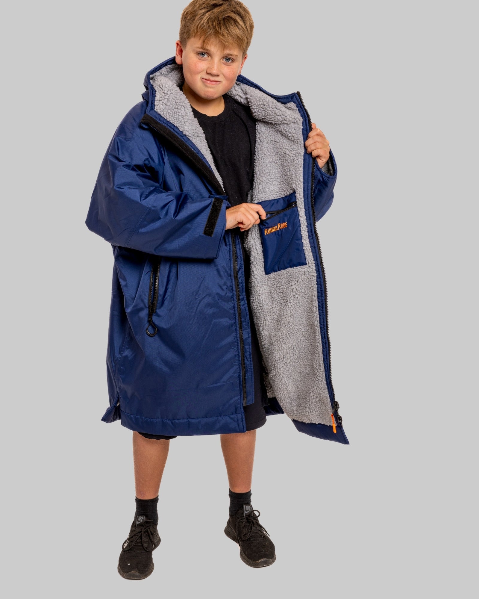 Child wearing a blue RugaRobe with grey fleece interior change robe on a grey background