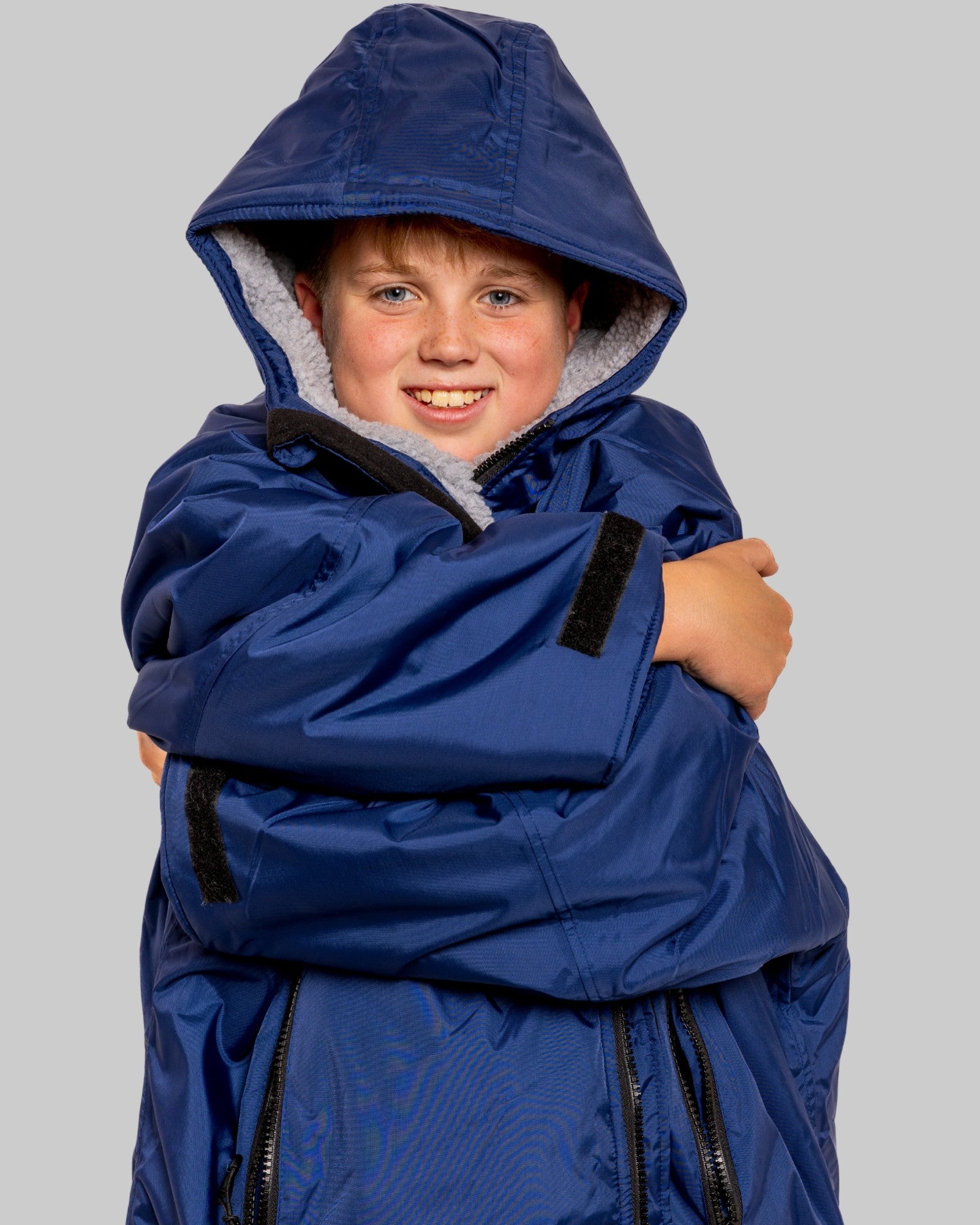 Child wearing a blue RuggaRobe with grey fleece interior change robe on a grey background