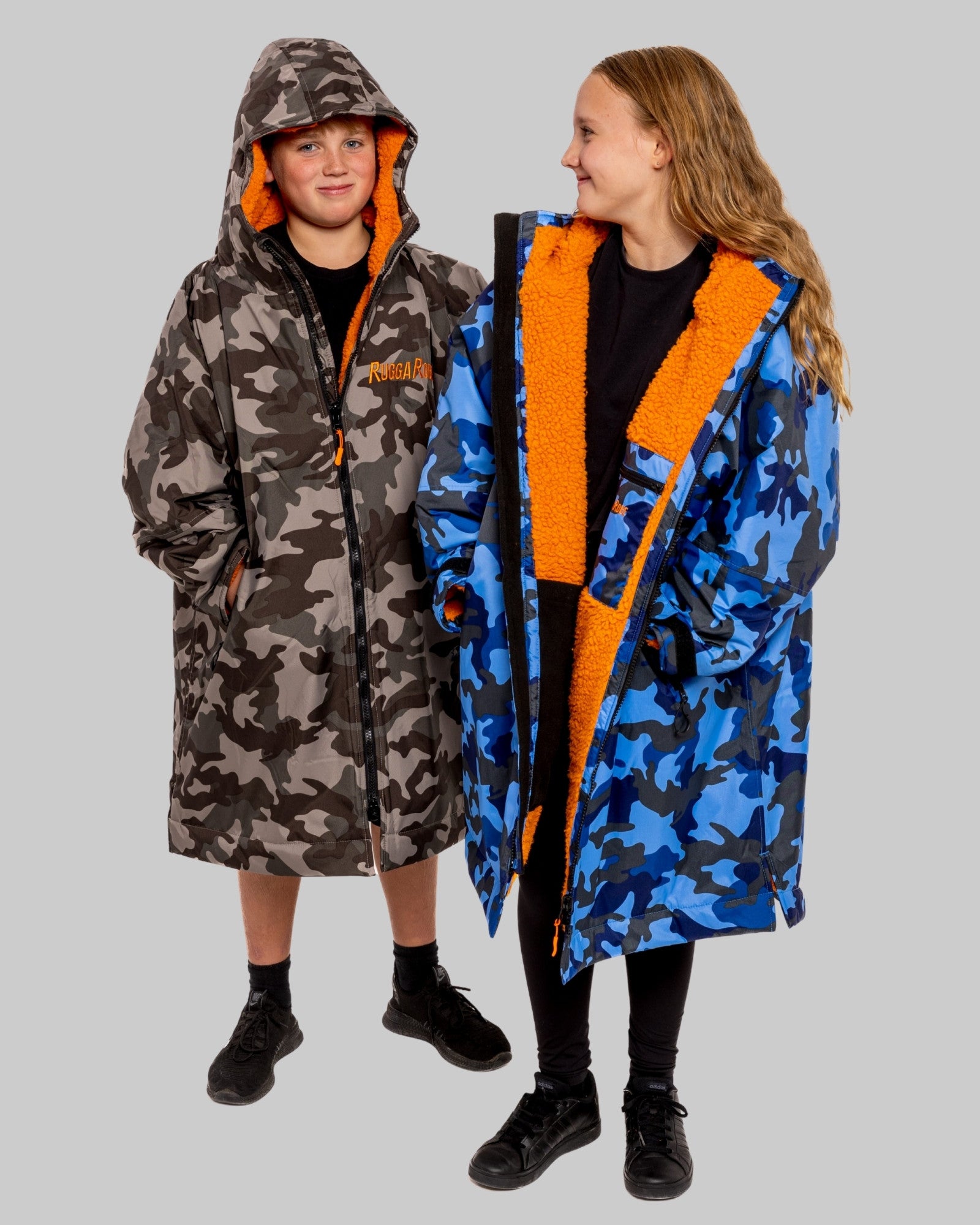 Two children wearing RuggaRobe change robes with camouflage patterns and orange accents on a gray background
