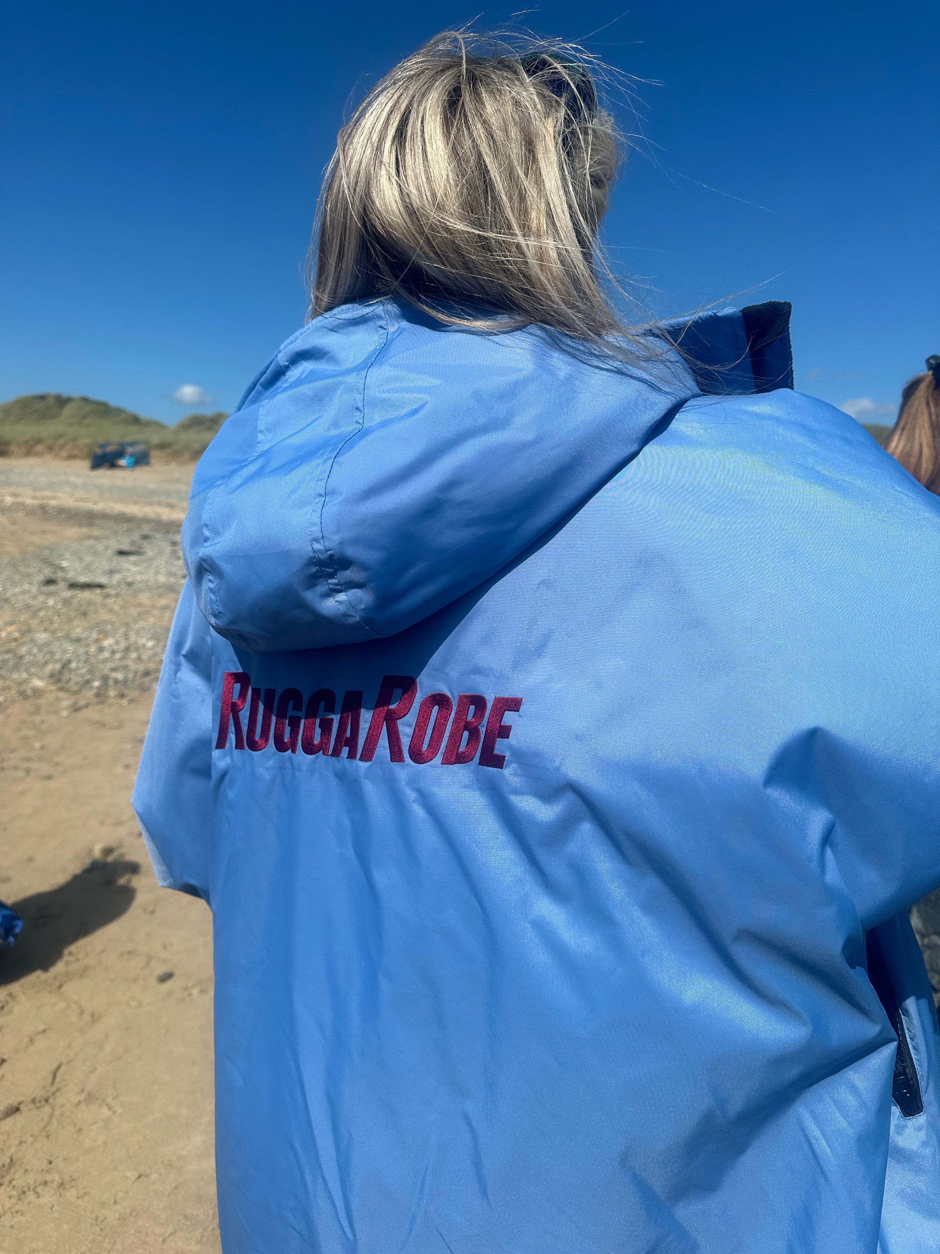 Person wearing a blue jacket with 'Ruggarobe' branding on a beach.
