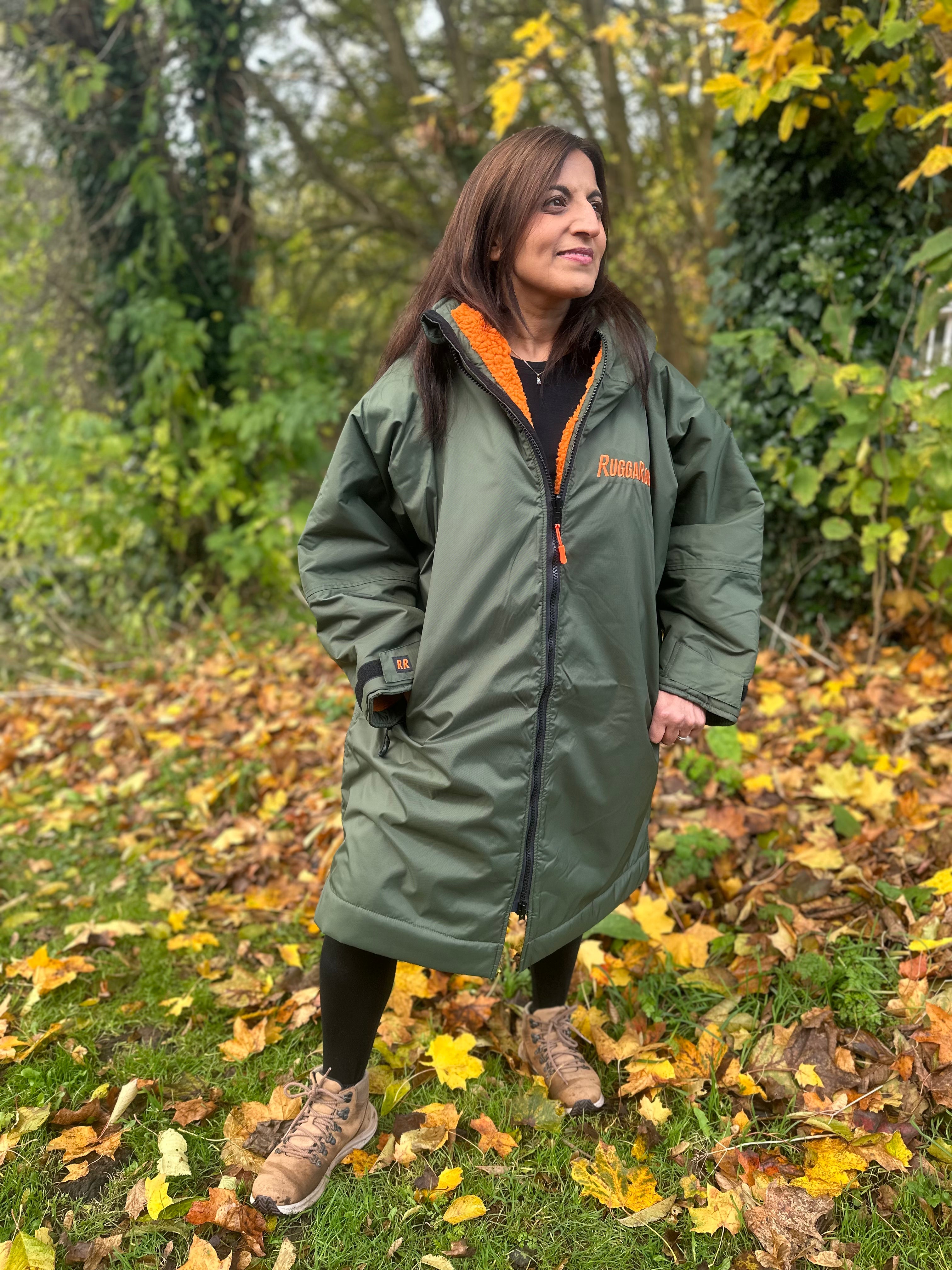 Person wearing a green ruggarobe with orange interior, outside walking through leaves