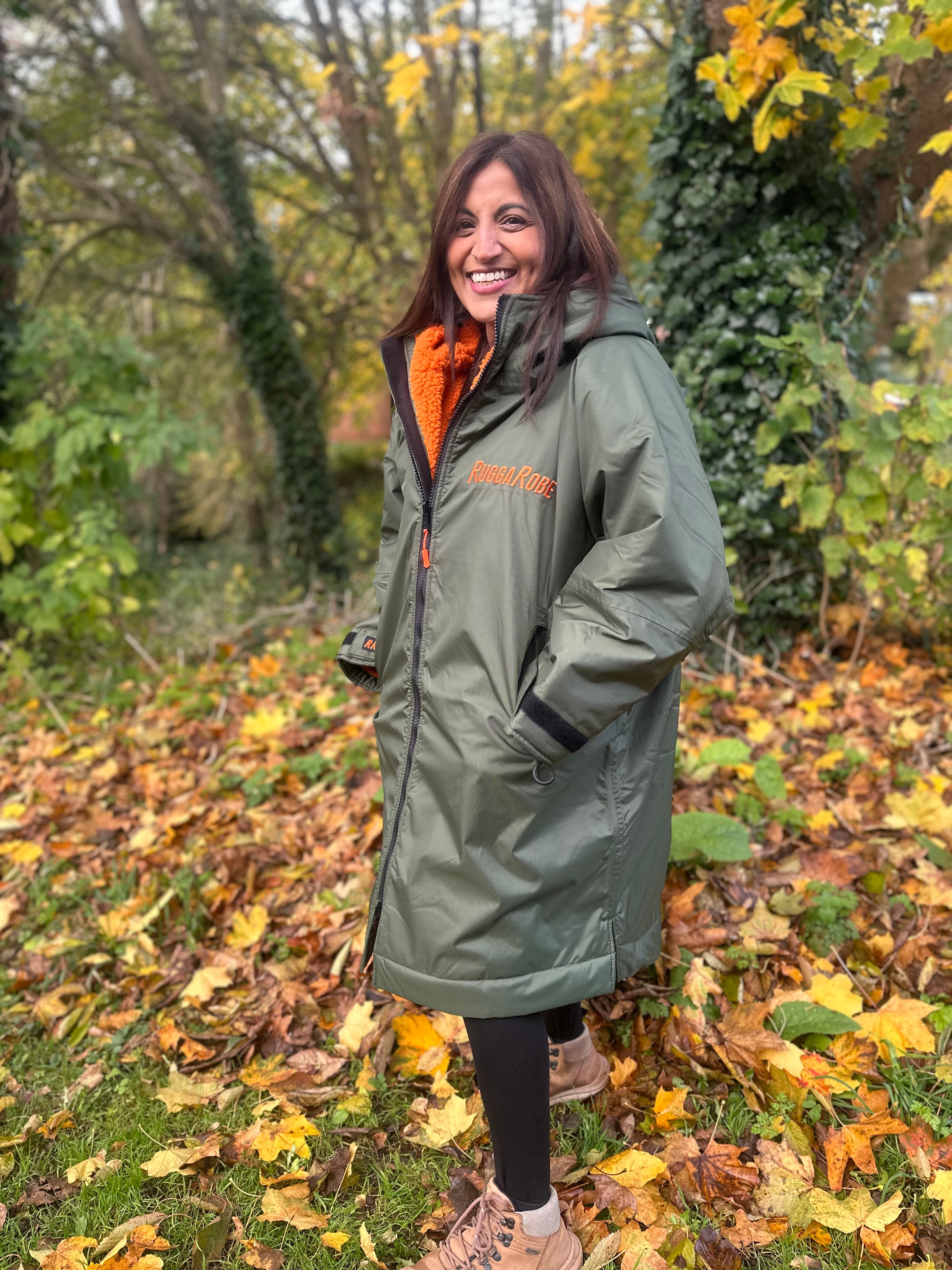 Person wearing a green ruggarobe with orange interior. Outside walking through leaves