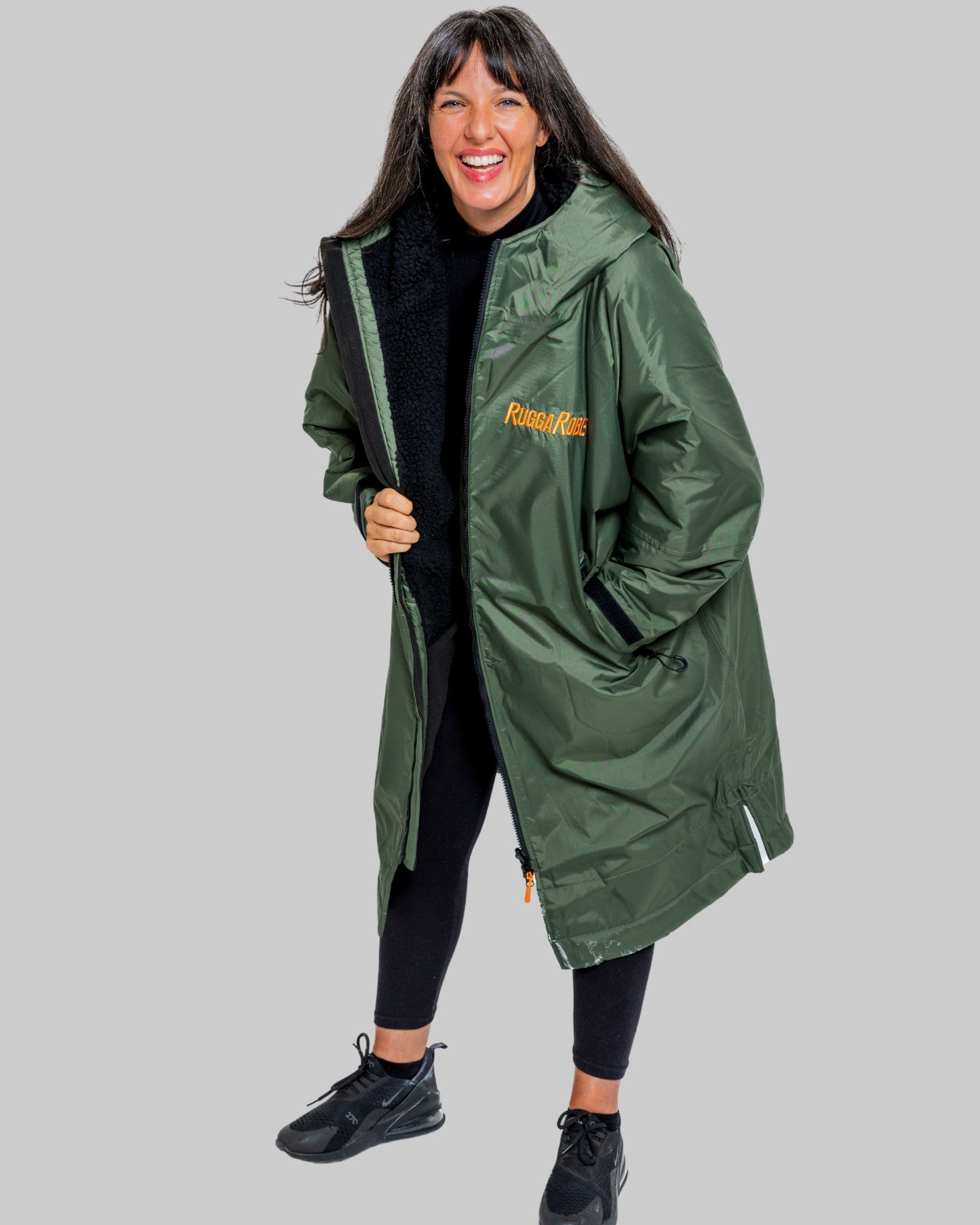 Woman wearing a green change robe with black fleece with a brand logo on a grey background